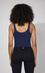 Woman wearing naval blue fitted tank top with built-in bra and black high-waisted leggings, back view.