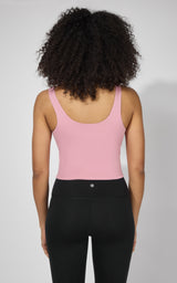 Women's pink tank top with built-in bra and scoop back, paired with black leggings.