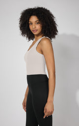 Light beige tank top with built-in bra, fitted silhouette on model with black leggings.