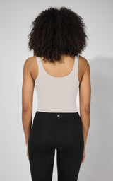 Women's beige tank top with built-in bra, scoop back, paired with black high-waisted pants.