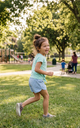 Toddler girl running outdoors in an aqua short-sleeve tee and light blue athletic shorts.