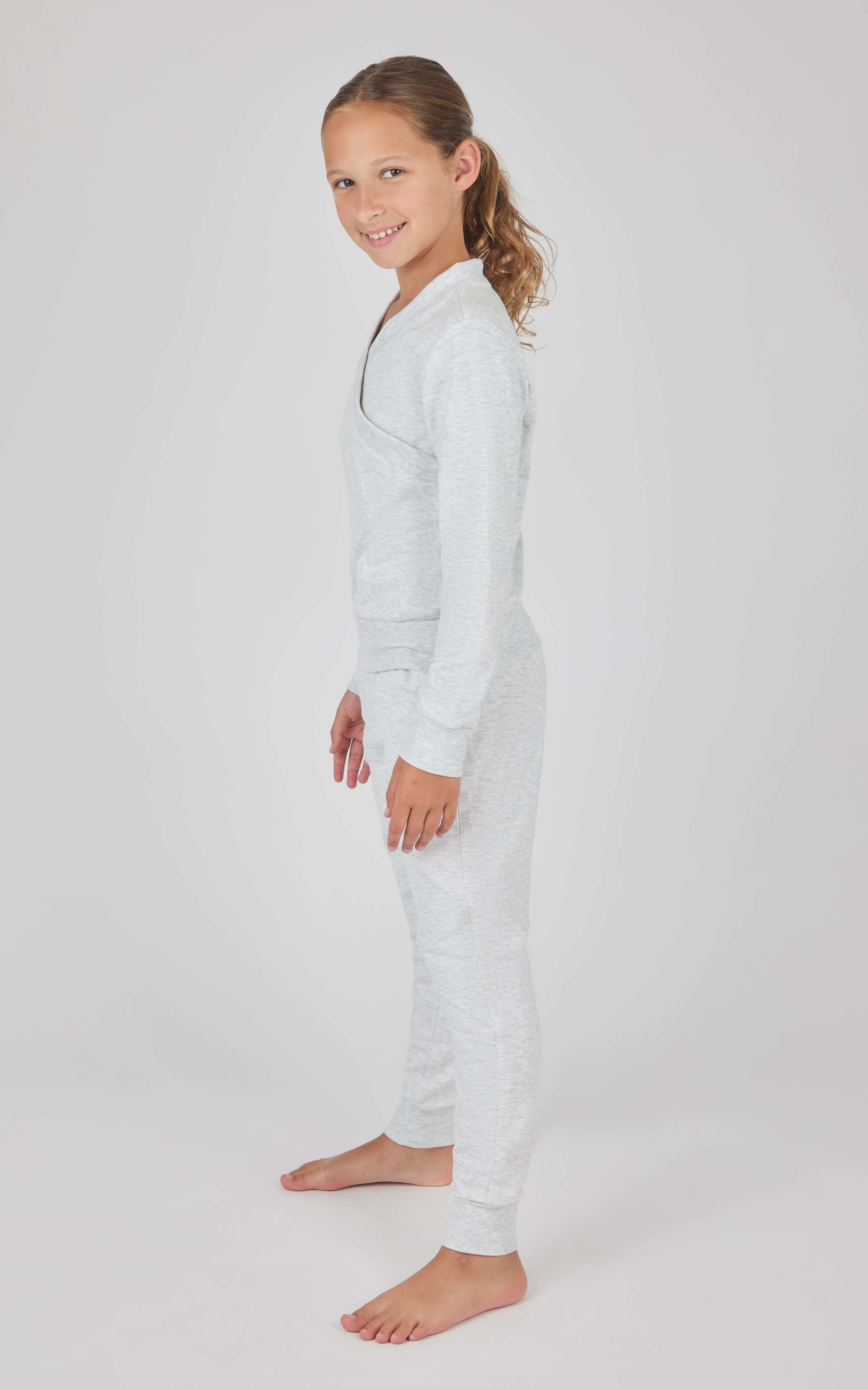 Girl wearing a white terry crossover long sleeve top and matching brushed joggers set, barefoot.