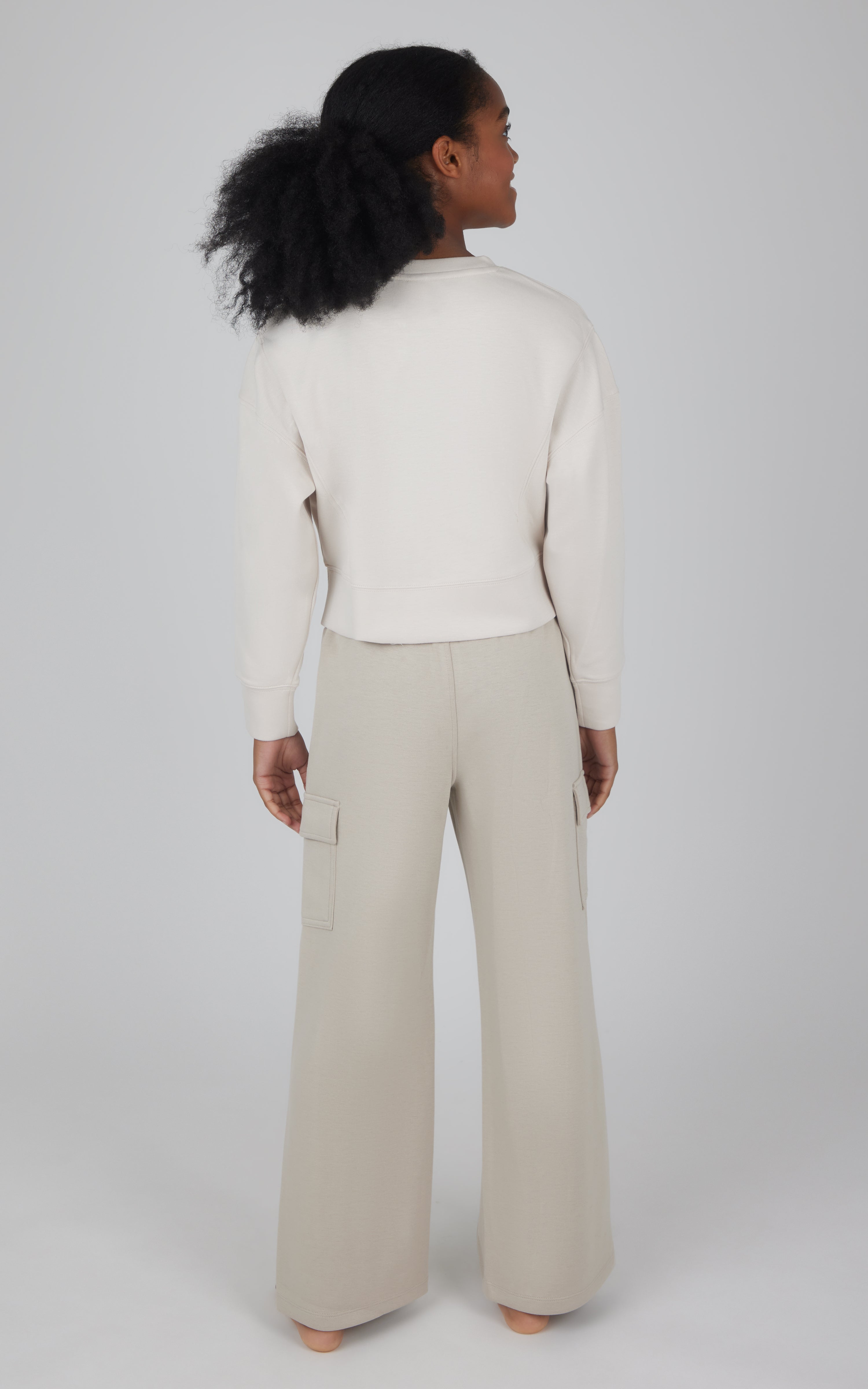 Girls softlite cream cropped pullover paired with beige wide-leg cargo pants from back view.