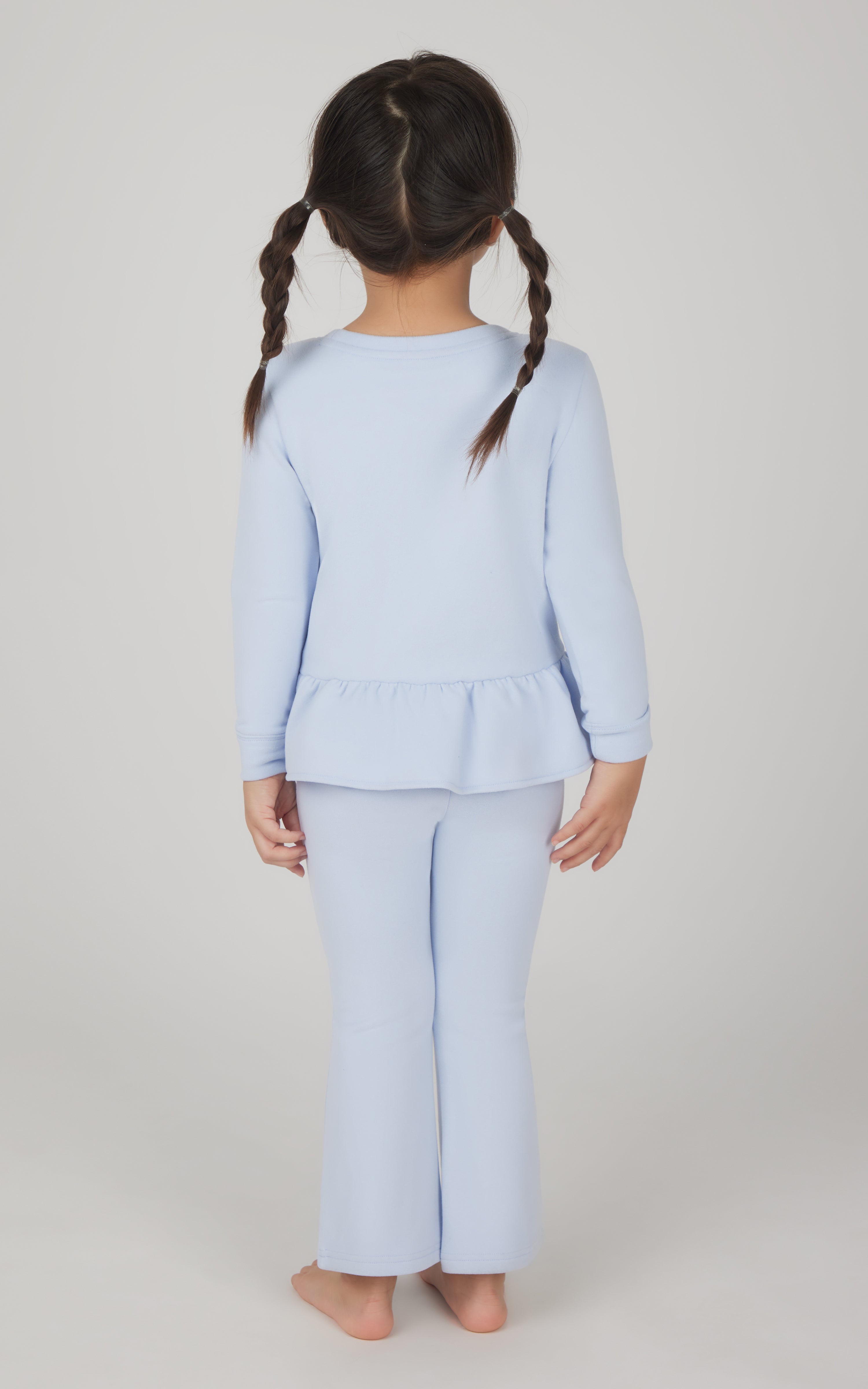 Toddler girl wearing light blue melange pullover top with ruffle hem and matching flare leg pants, back view.