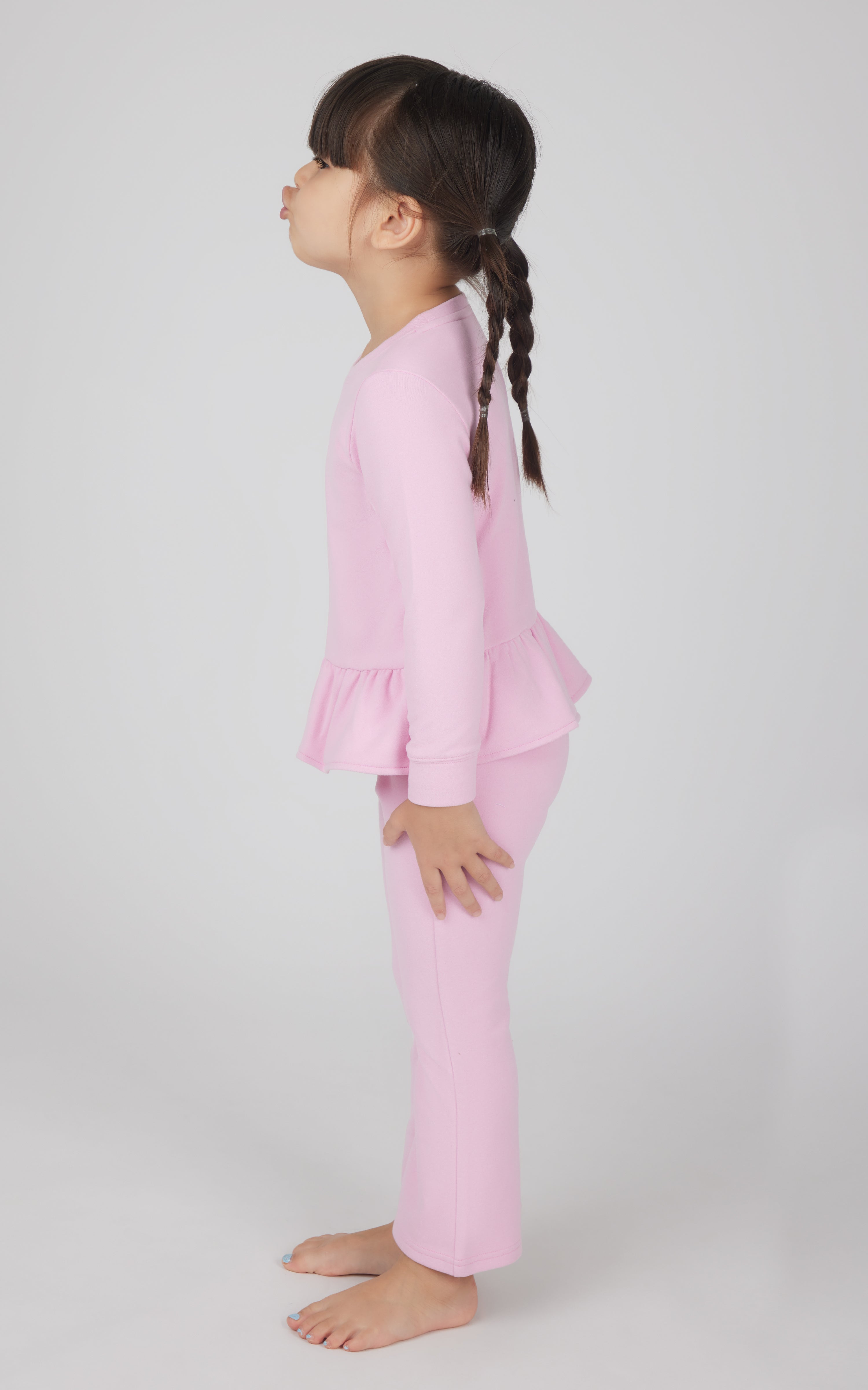 Toddler girl wearing pink pullover top with ruffled hem and matching flare leg pants.