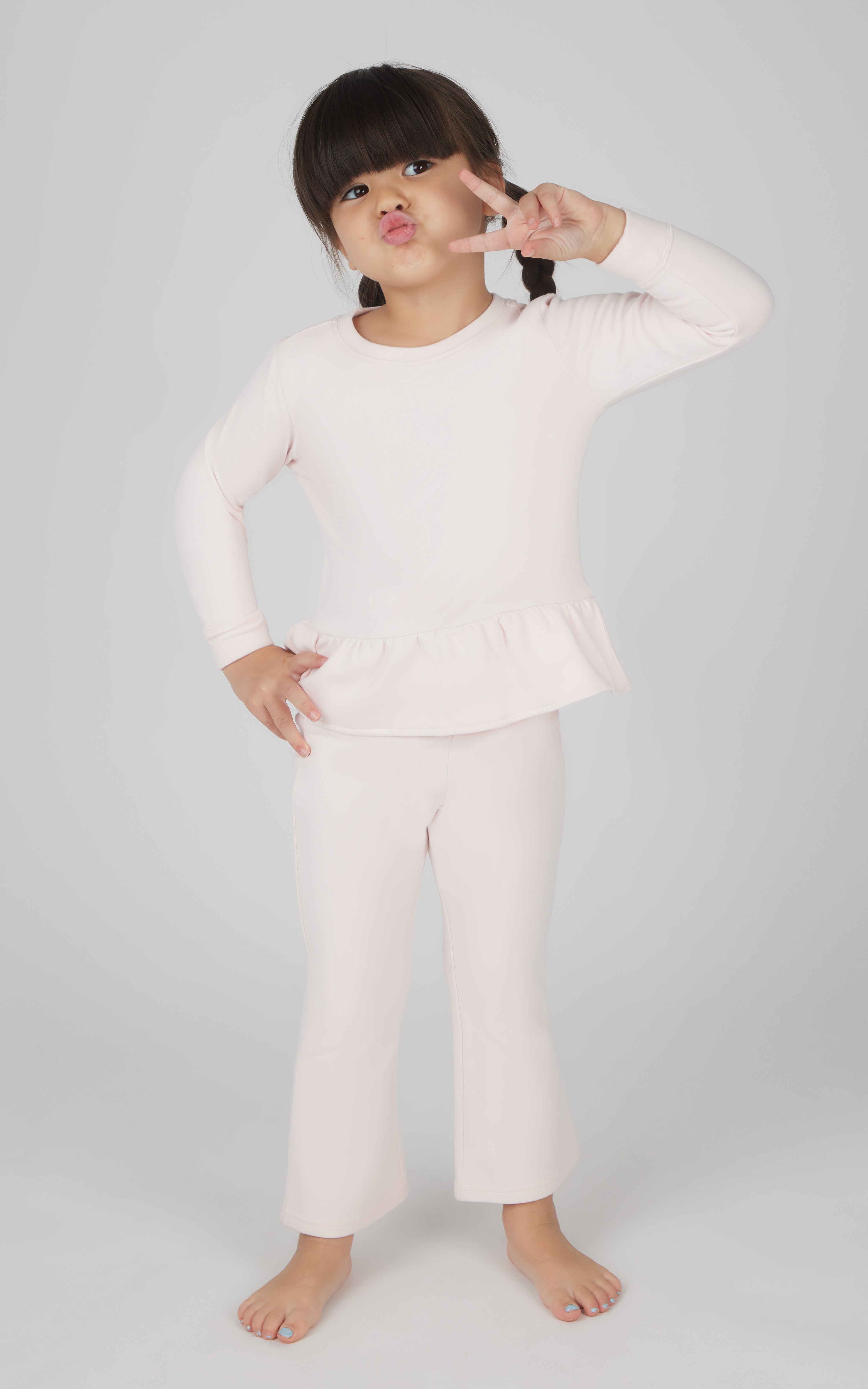Toddler girl wearing light pink melange pullover top with peplum hem and matching flare leg pants.