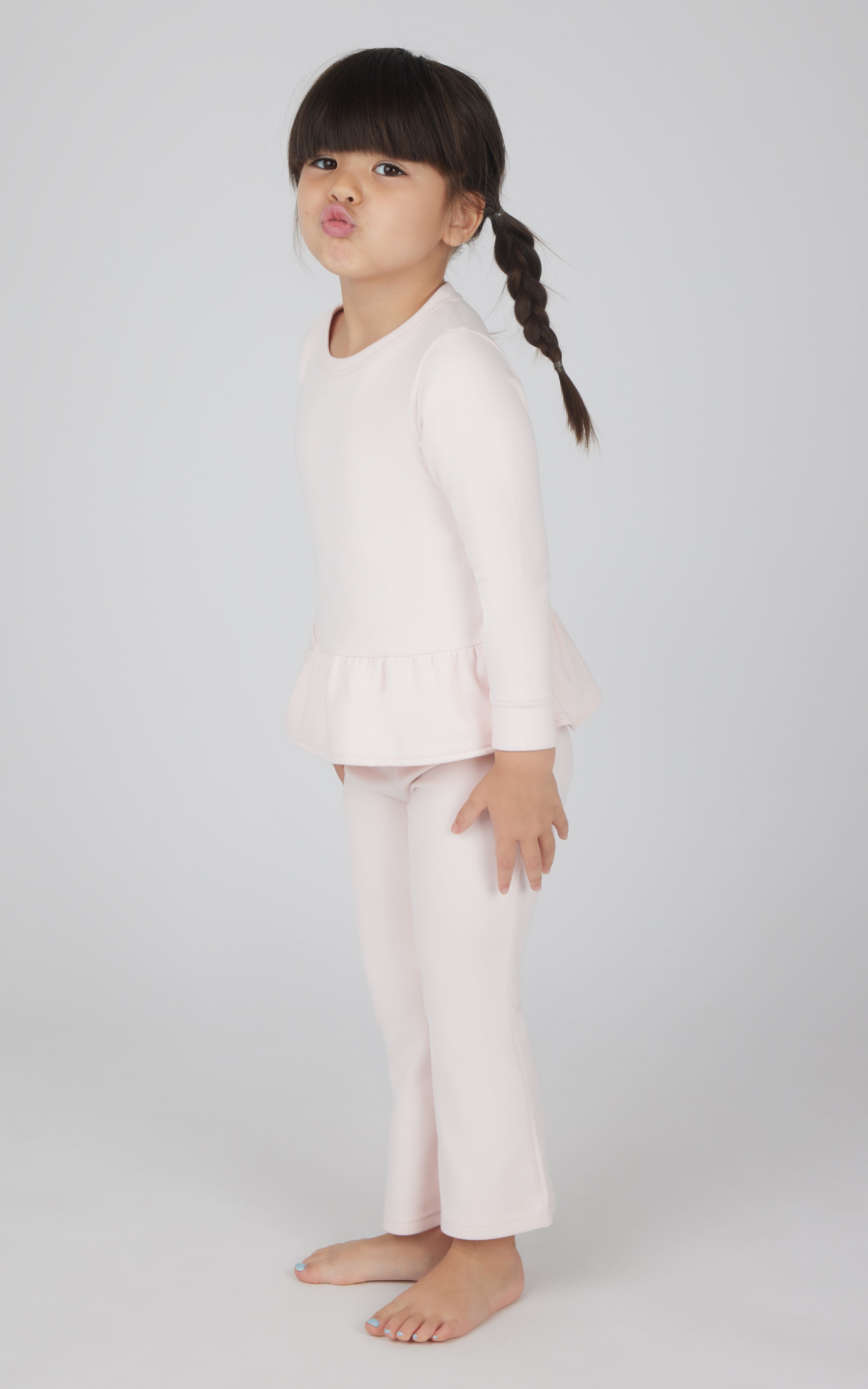 Toddler girl wearing light pink melange pullover top with ruffle hem and matching flare leg pants.