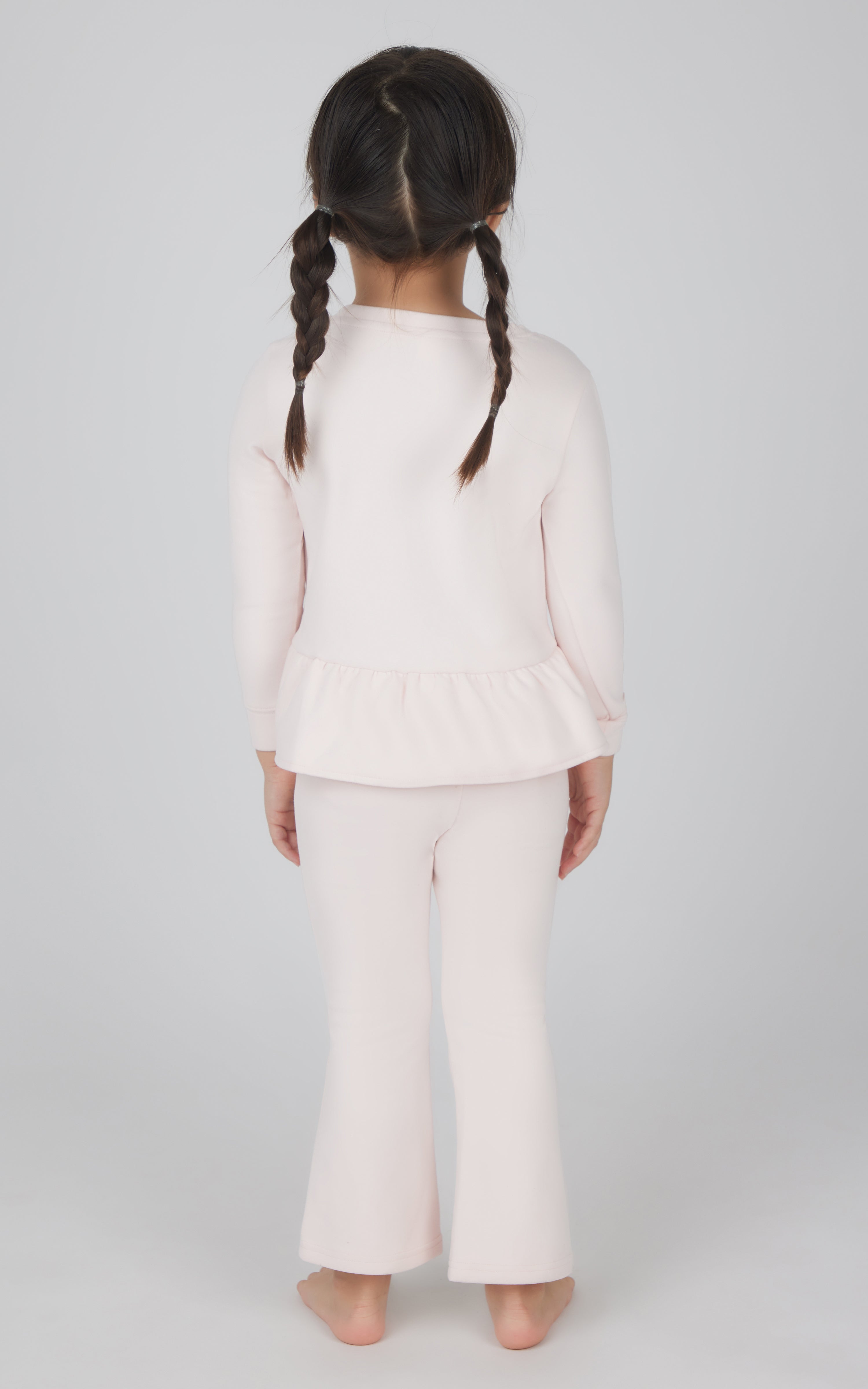 Toddler girl wearing light pink melange pullover with ruffle hem and matching flare leg pants, back view.