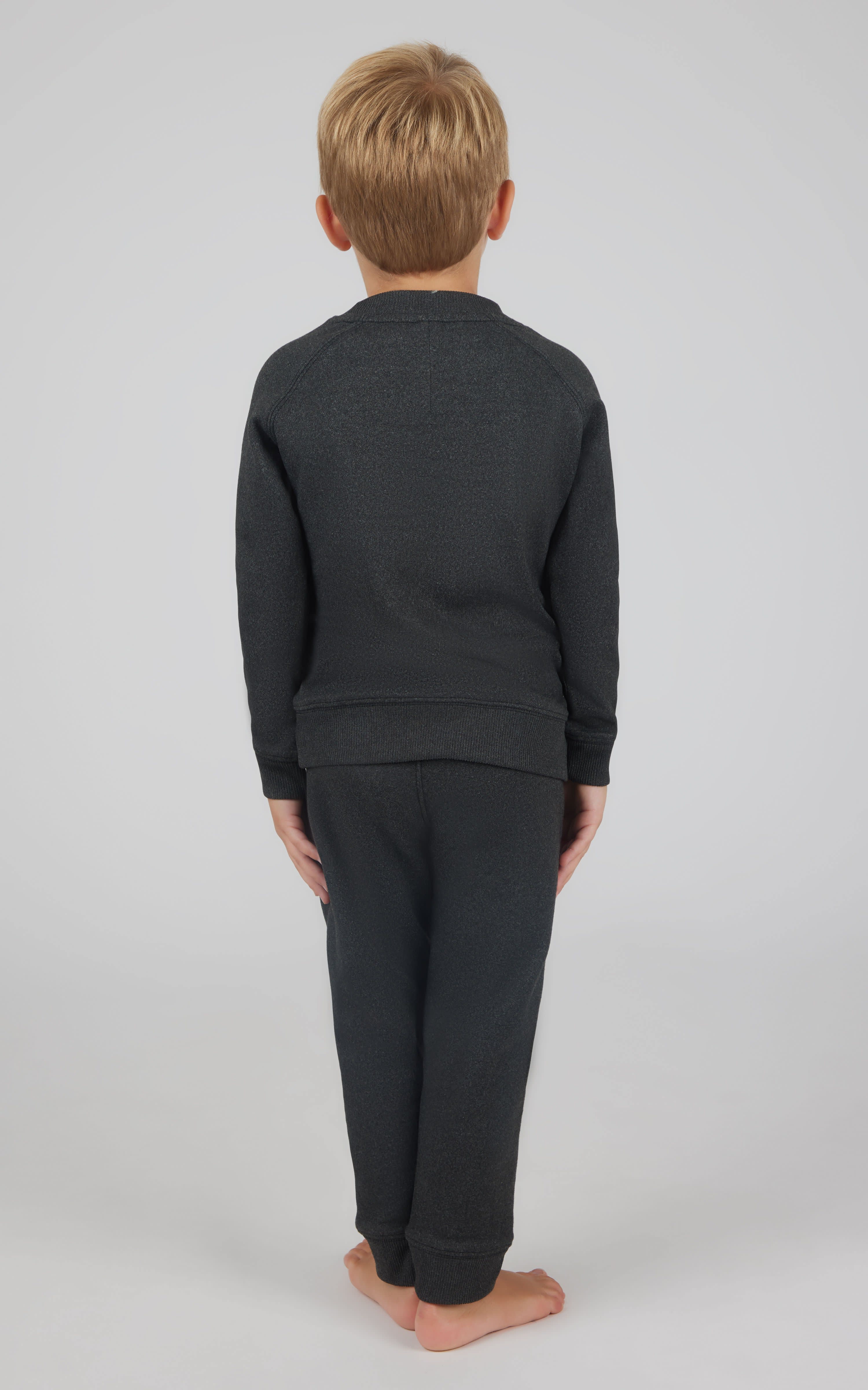 Toddler boy wearing black fleece sweatshirt and joggers set, standing barefoot with back facing camera.
