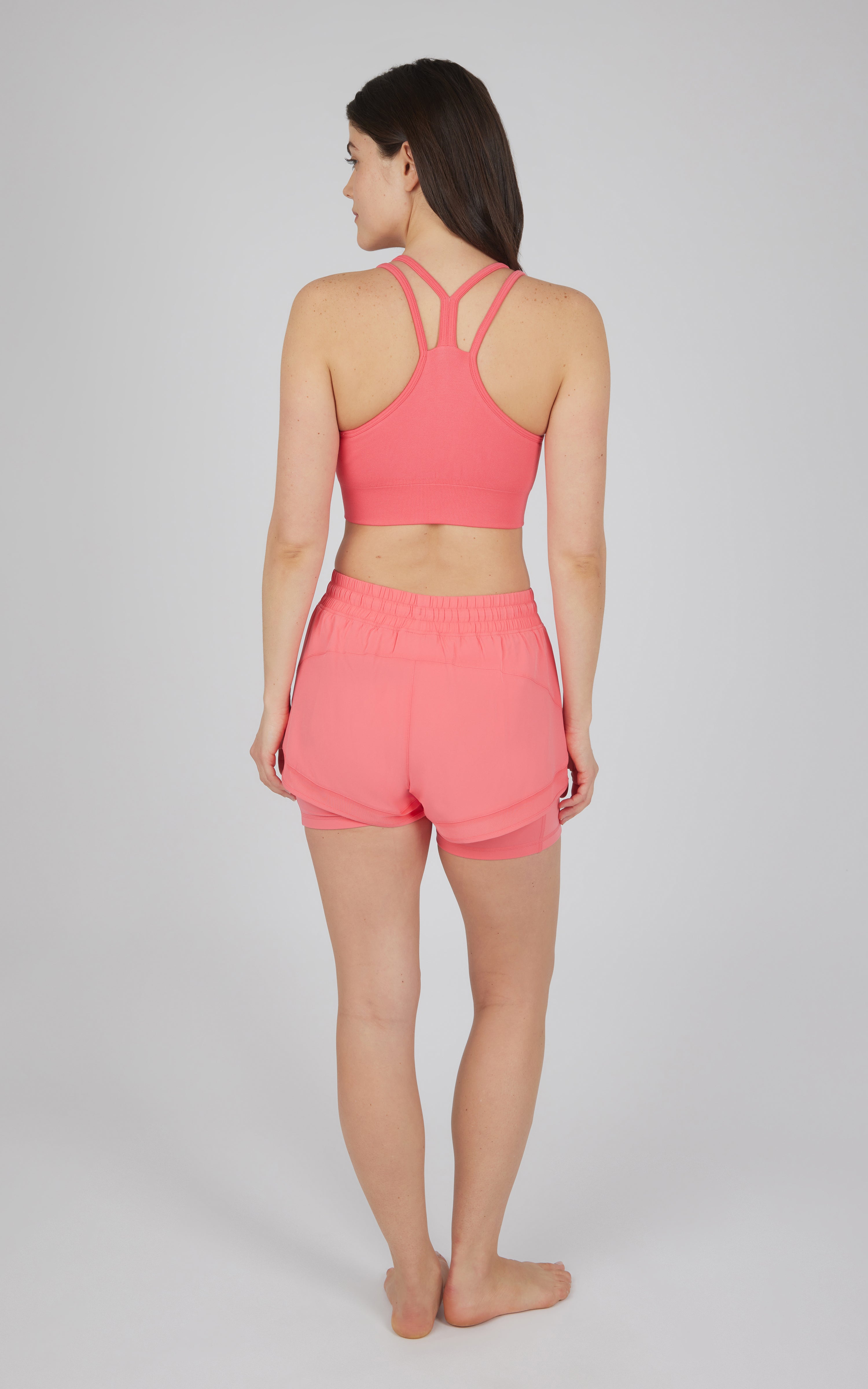 Seamless coral longline sports bra with crisscross back straps and matching coral running shorts with elastic waistband.