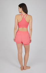 Seamless coral longline sports bra with crisscross back straps and matching coral running shorts with elastic waistband.
