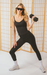 Woman wearing a black scoop-neck bra tank and matching high-waisted ankle leggings, posed with dumbbells.