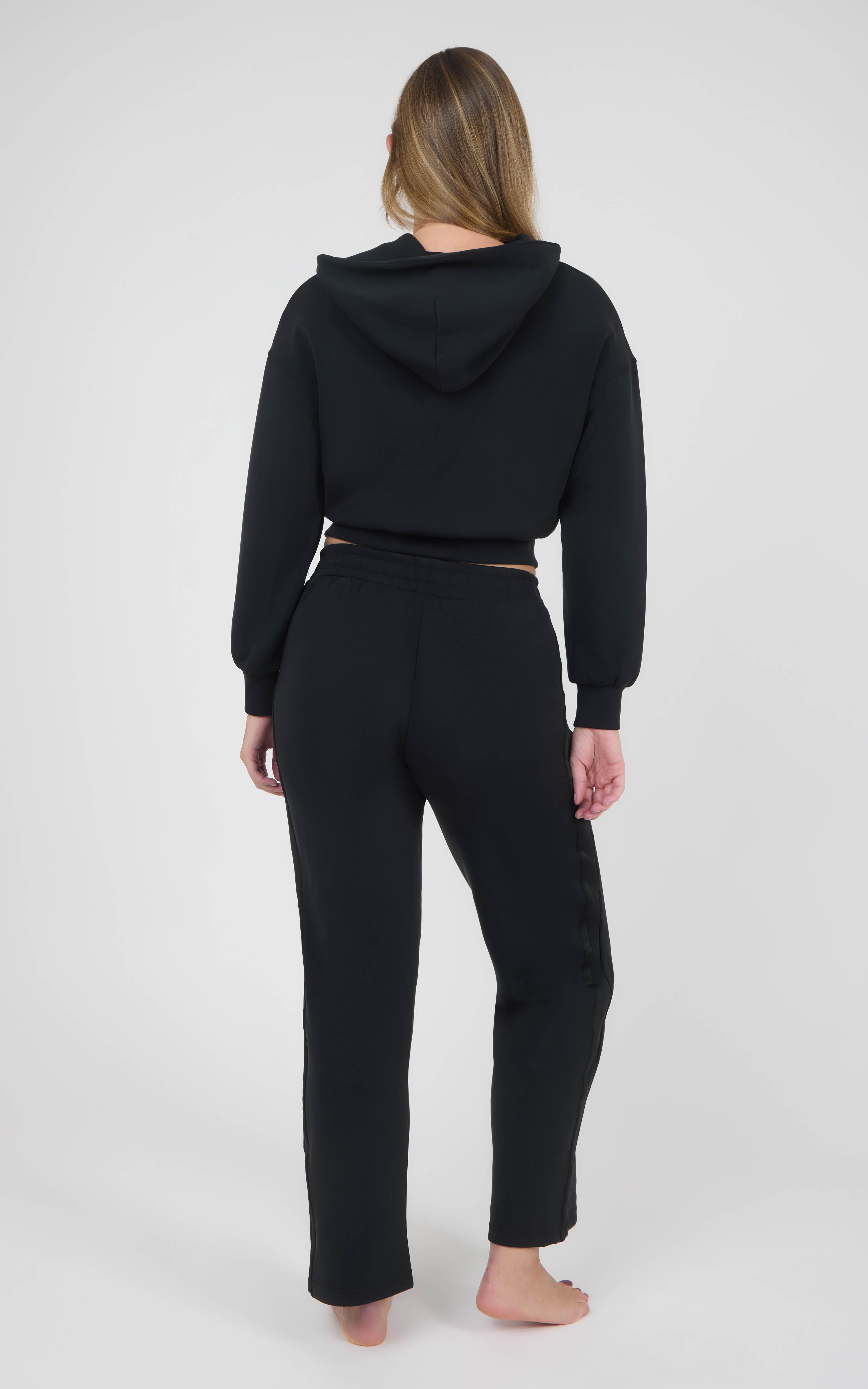 Black women’s matching set with a cropped hooded jacket and relaxed straight-leg pants, shown from the back.