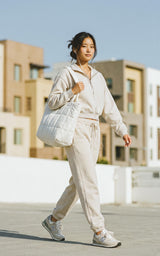 Woman wearing a cream half-zip lounge top and foldover joggers with a matching quilted shoulder bag.