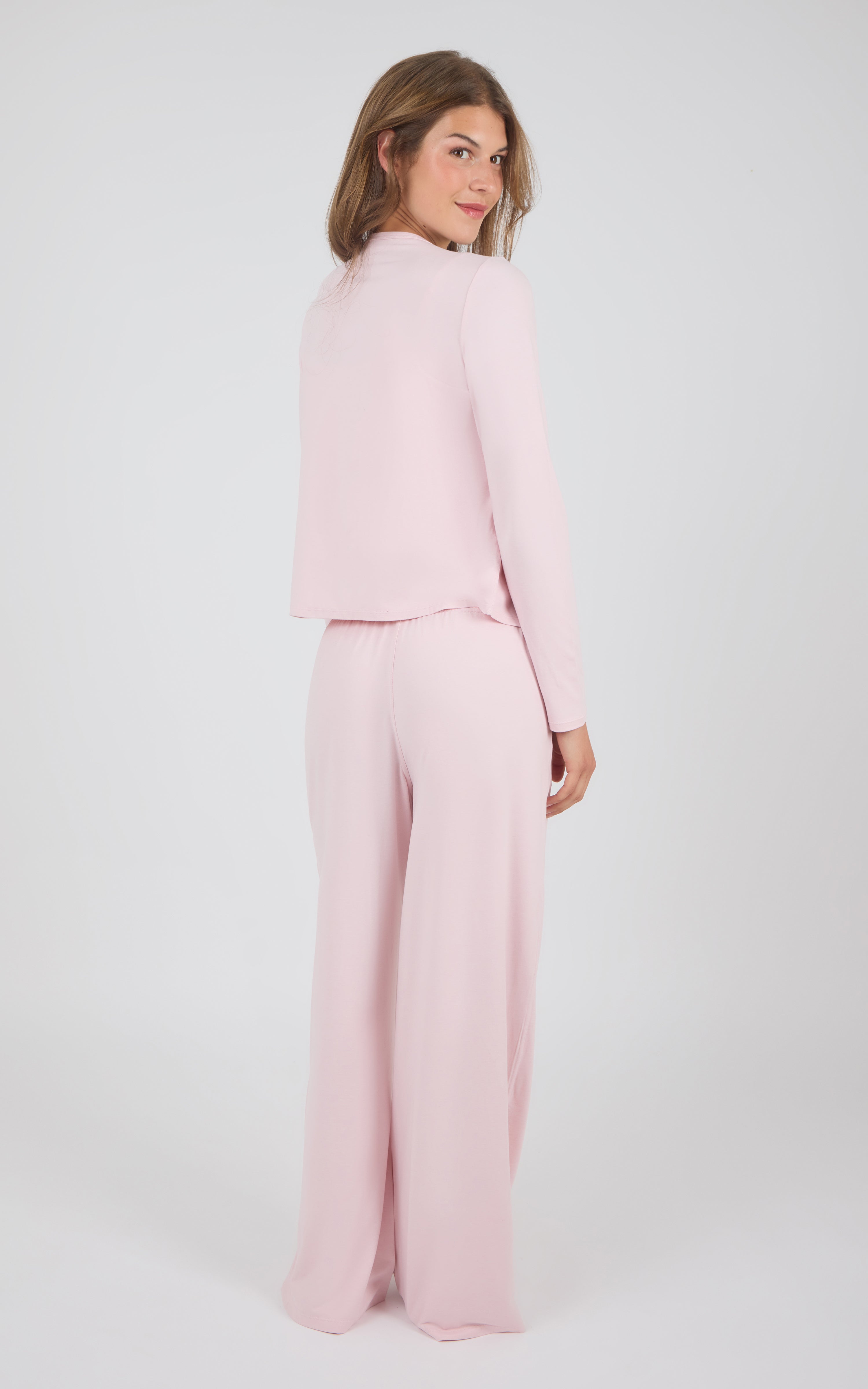 A woman modeling a light pink two-piece outfit consisting of a cropped long-sleeve top and matching wide-leg trousers, photographed against a plain light gray studio background.