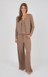 A woman modeling a matching lounge set consisting of a cropped button-front cardigan, a ribbed tank top, and wide-leg drawstring pants in a solid taupe-brown color, shot against a light gray studio background.