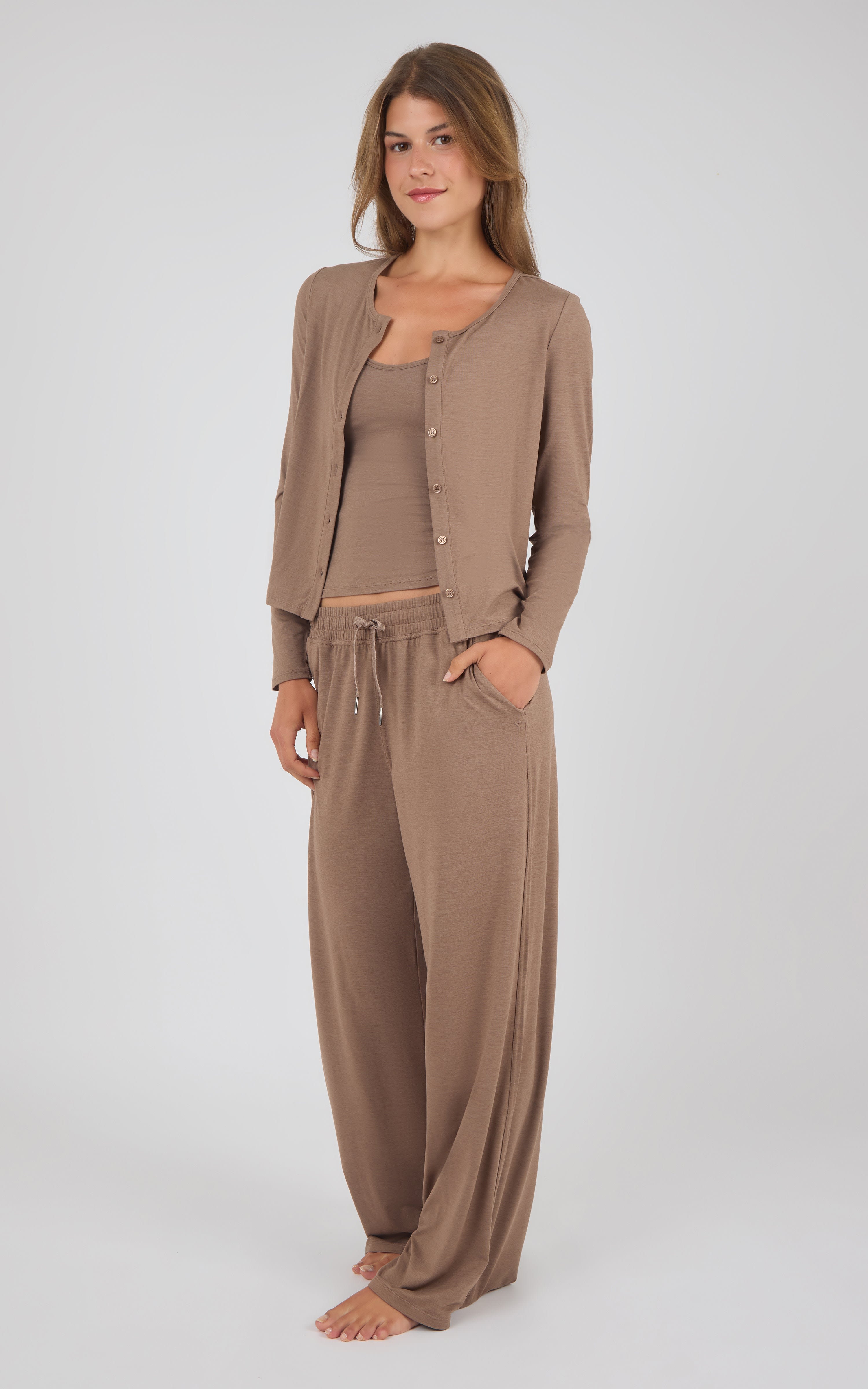 A woman modeling a matching lounge set consisting of a taupe cardigan, tank top, and drawstring pants against a light gray studio background.