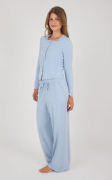 A woman modeling a light blue two-piece loungewear set consisting of a long-sleeve cardigan top and matching wide-leg pants, photographed against a plain light gray studio background.