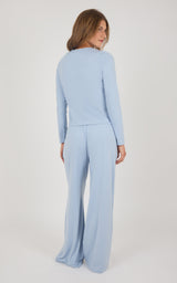 A woman wearing a light blue long-sleeve jumpsuit, photographed from the back against a plain light gray studio background.