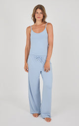 A woman modeling a light blue two-piece loungewear set consisting of a sleeveless camisole top and matching wide-leg drawstring pants, shot against a neutral light gray studio background.