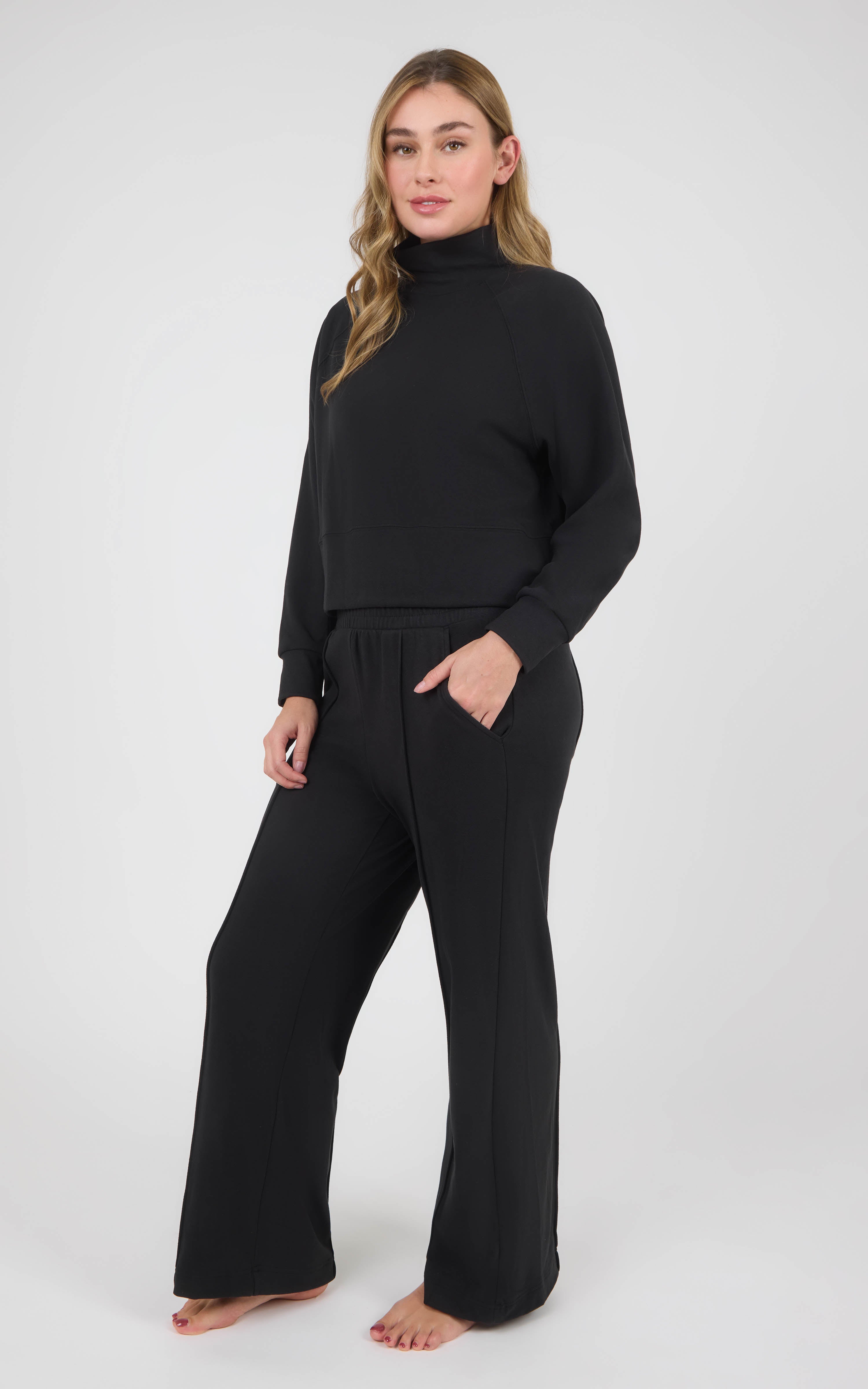Model wearing a black long-sleeve pullover with a high neckline and matching wide-leg pants, styled barefoot.