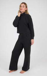 Black marled pique pullover with long raglan sleeves and matching pintuck wide-leg pants, modeled with bare feet.