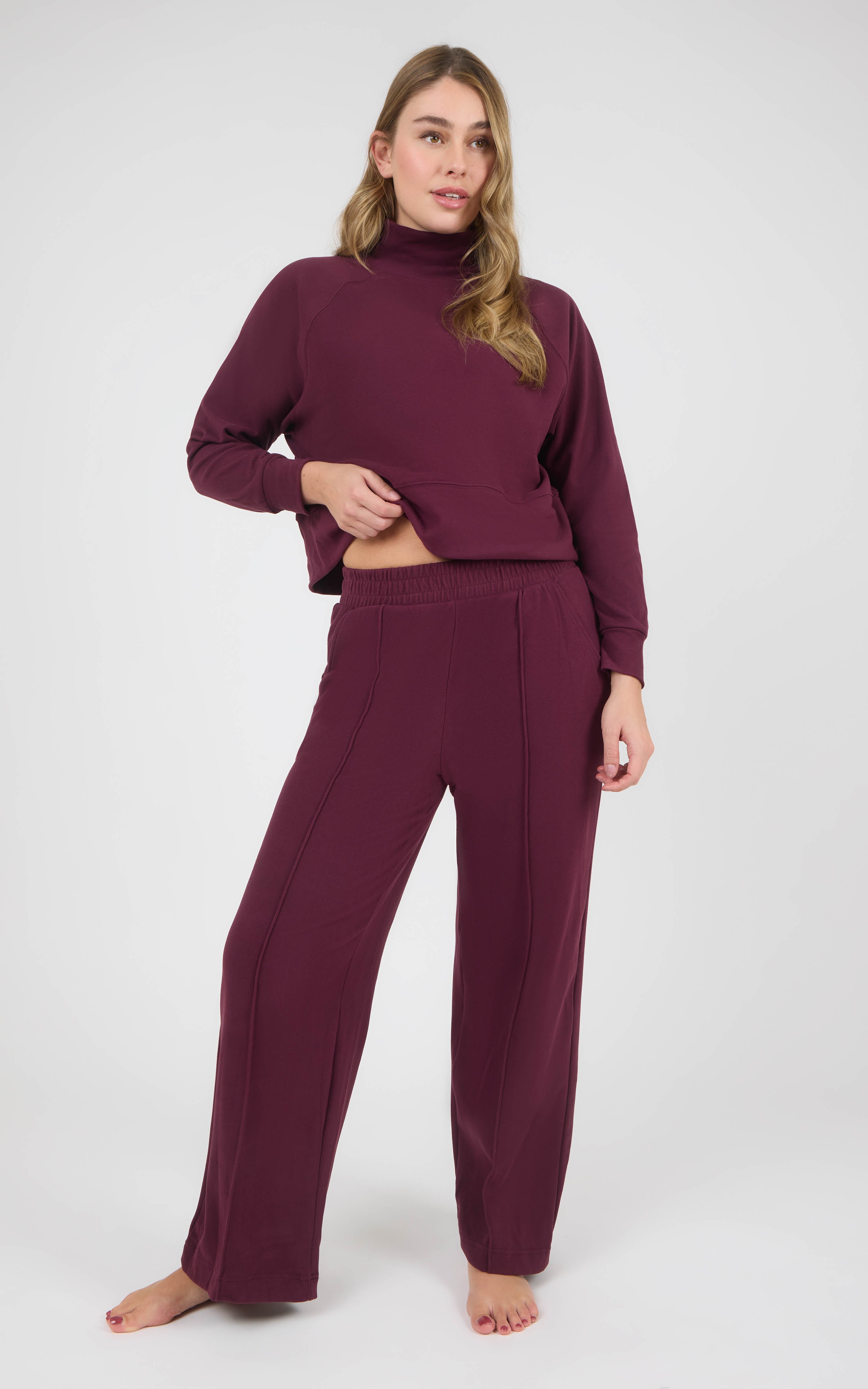 Woman wearing a burgundy marled pique pullover with long sleeves and matching wide-leg pants, styled barefoot.