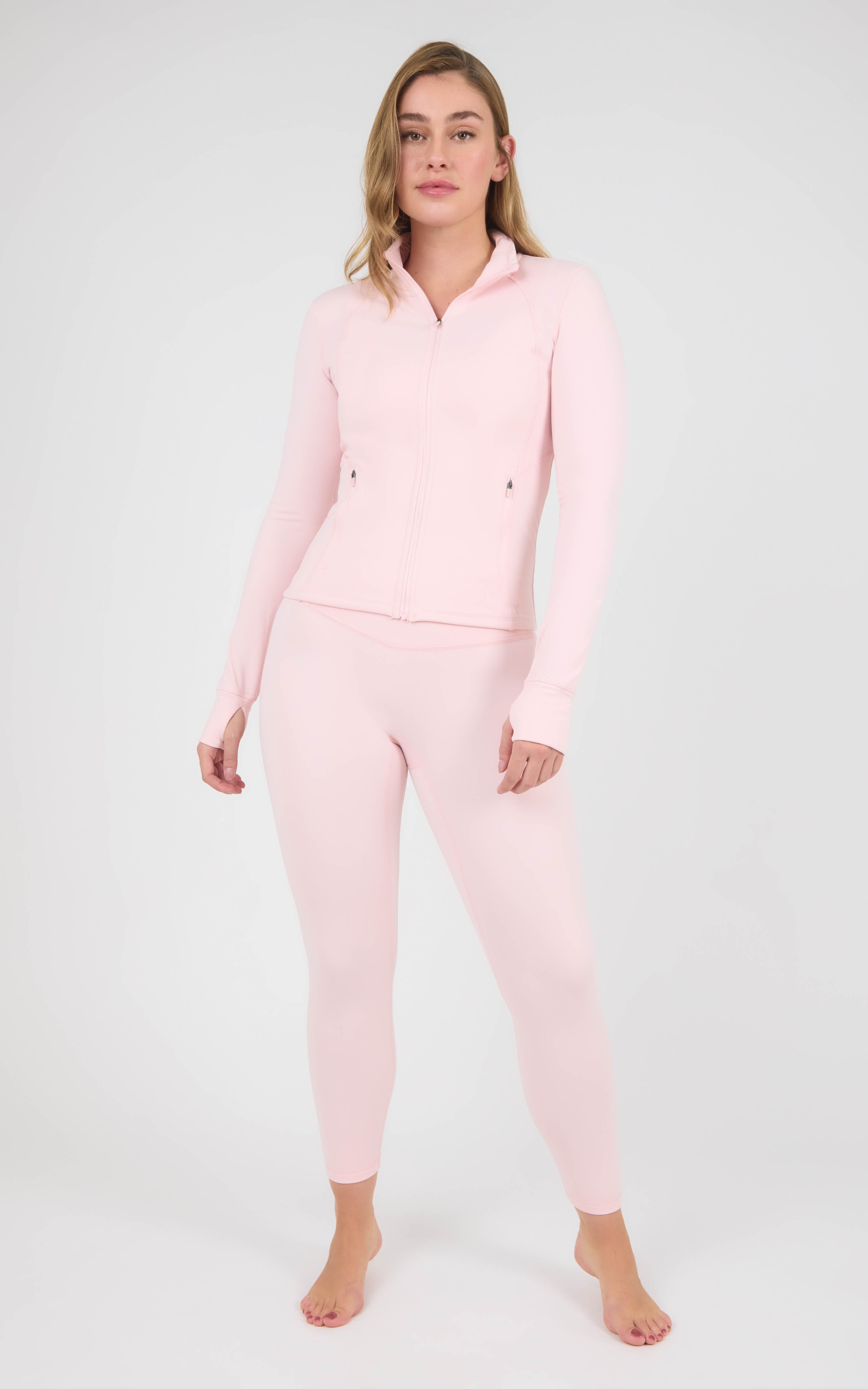 Woman wearing a pale pink fitted zip-front jacket and matching ankle-length leggings with a V-shaped waistband.