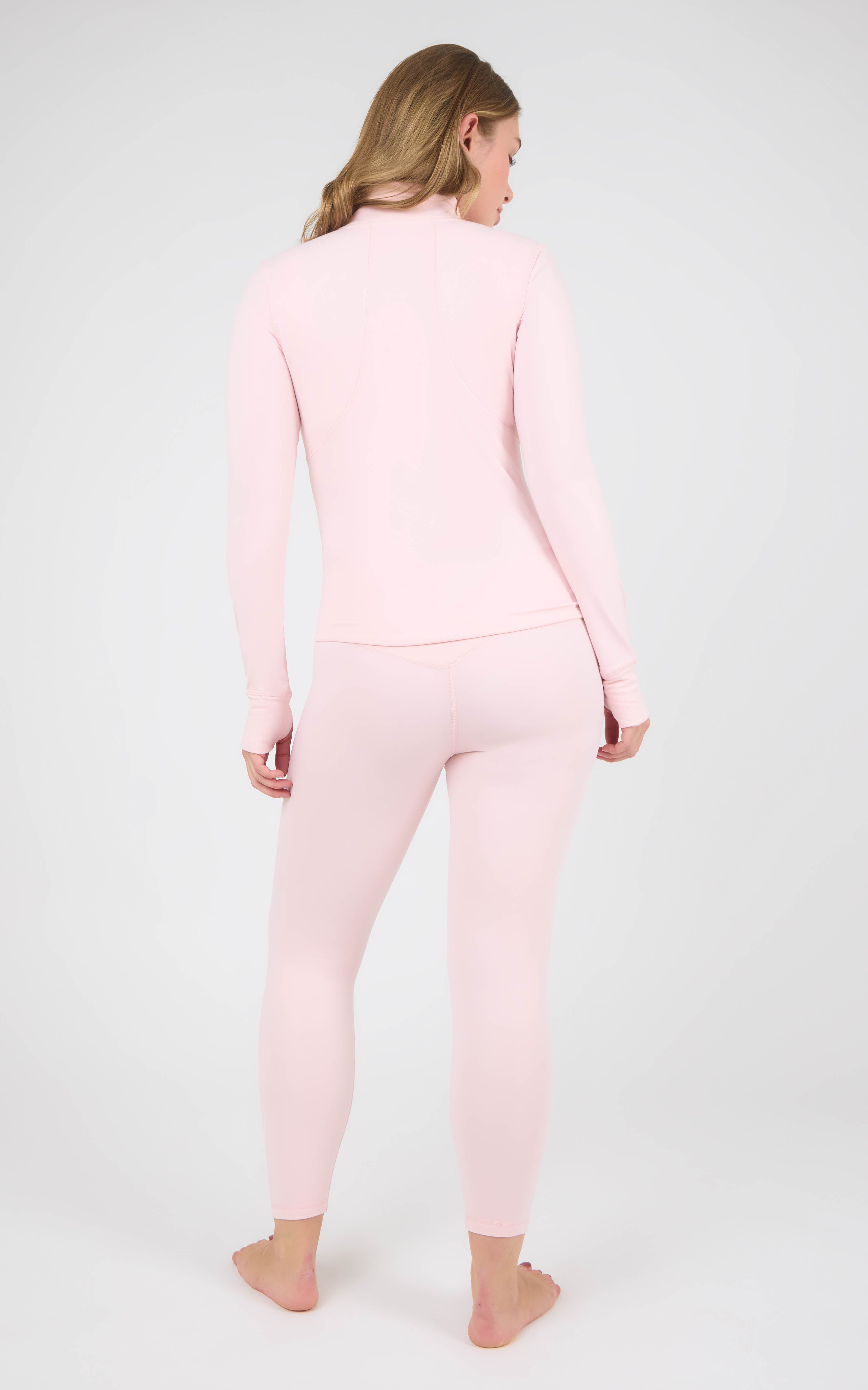 Back view of a woman wearing a pale pink fitted jacket and matching ankle-length leggings.