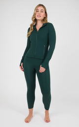 Woman wearing a dark forest-green zip-up jacket and matching high-waisted ankle leggings, shown full-length against a plain.