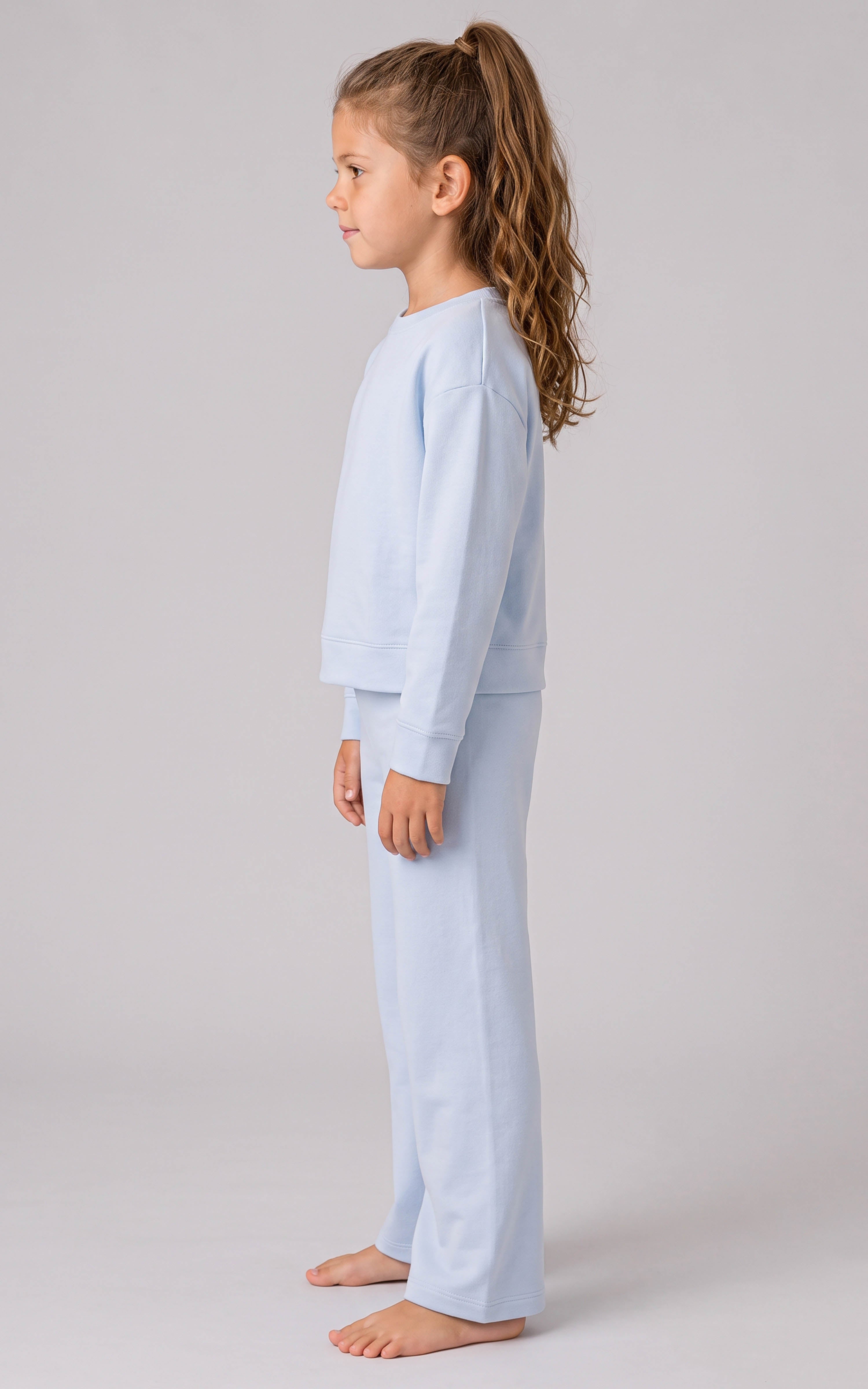 Girl wearing a pale blue ribbed three-piece lounge set with a relaxed long-sleeve top and loose, slit-hem pants.