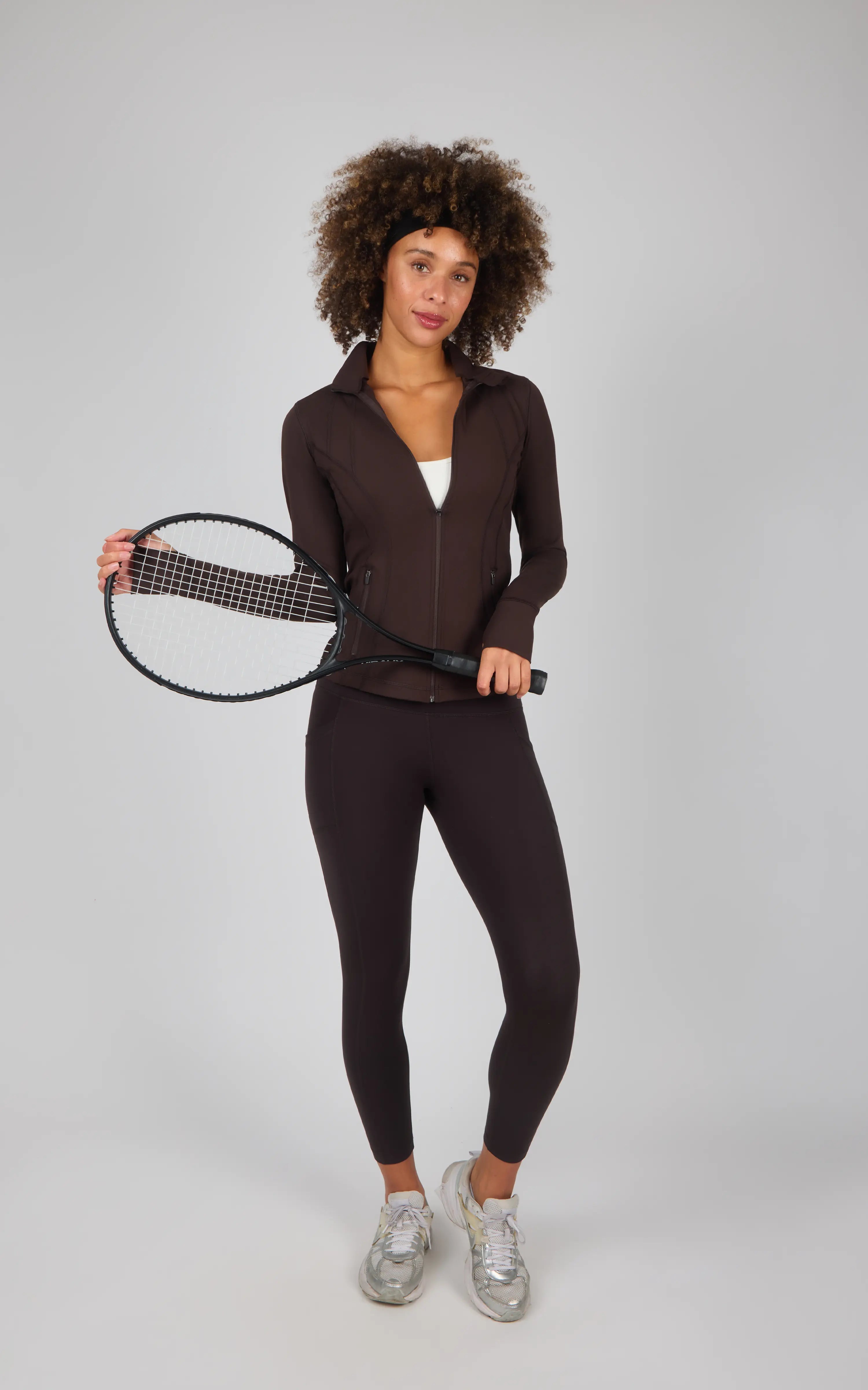 Black ankle-length leggings with a high waistband and side pocket, paired with a matching fitted zip-up top, worn with.