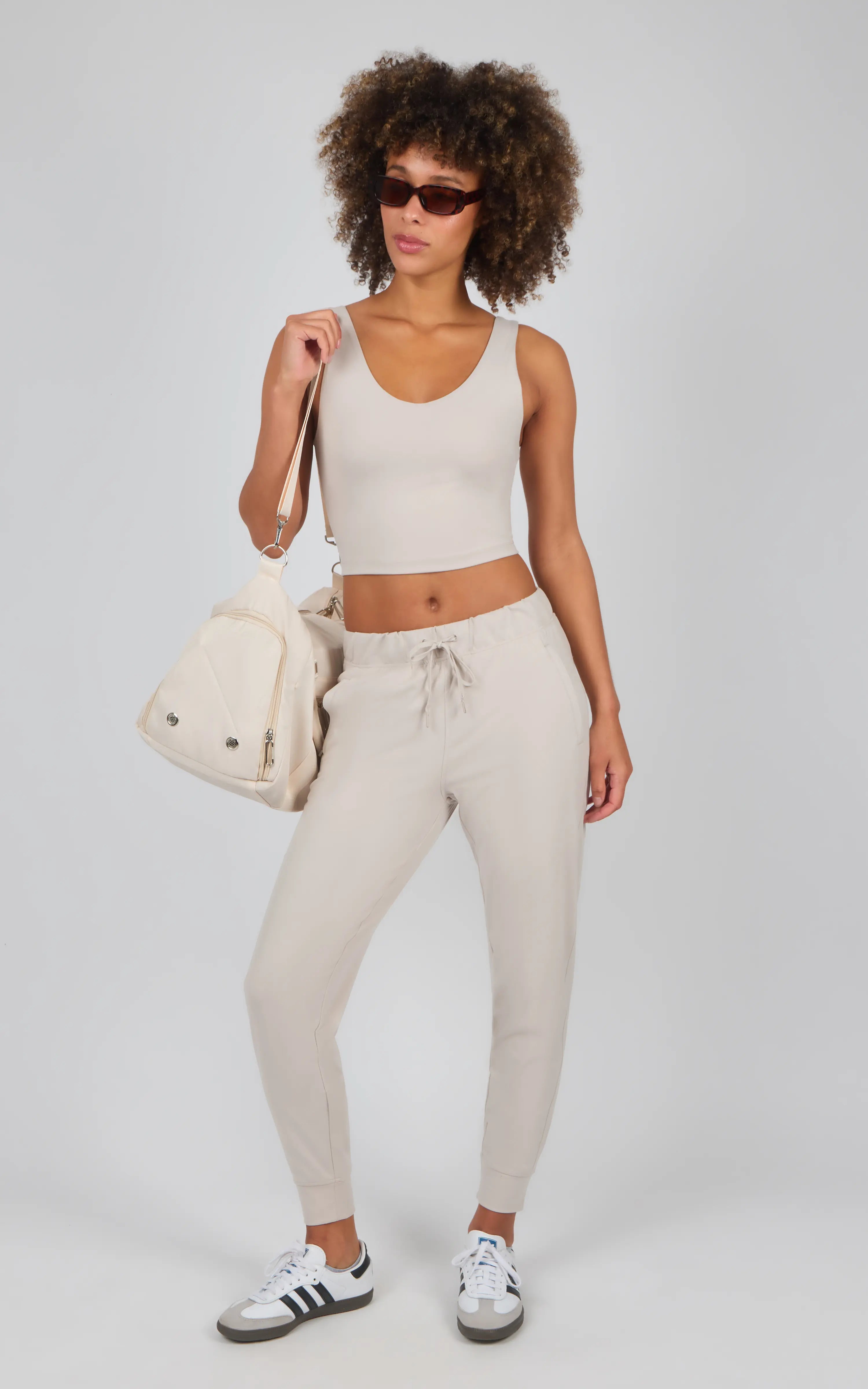 Light beige jogger pants with side pockets, slim fit, and drawstring waist, paired with a white cropped tank and white.