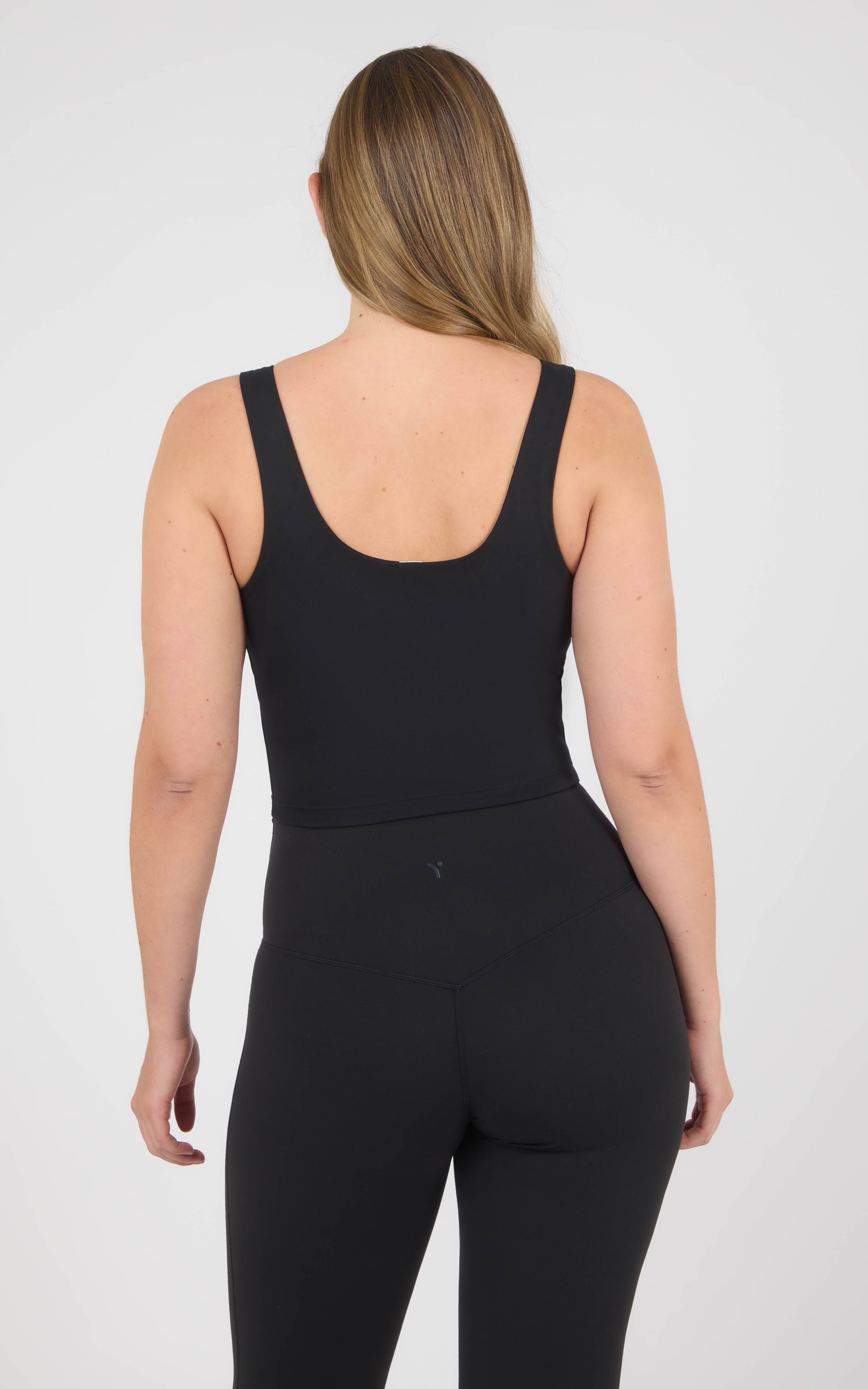 Model wearing a black cropped tank with wide straps, a scoop back, and a fitted built-in bra.