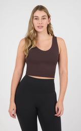 Woman wearing a cropped chocolate-brown scoop-neck tank with a built-in bra and black high-waisted leggings.