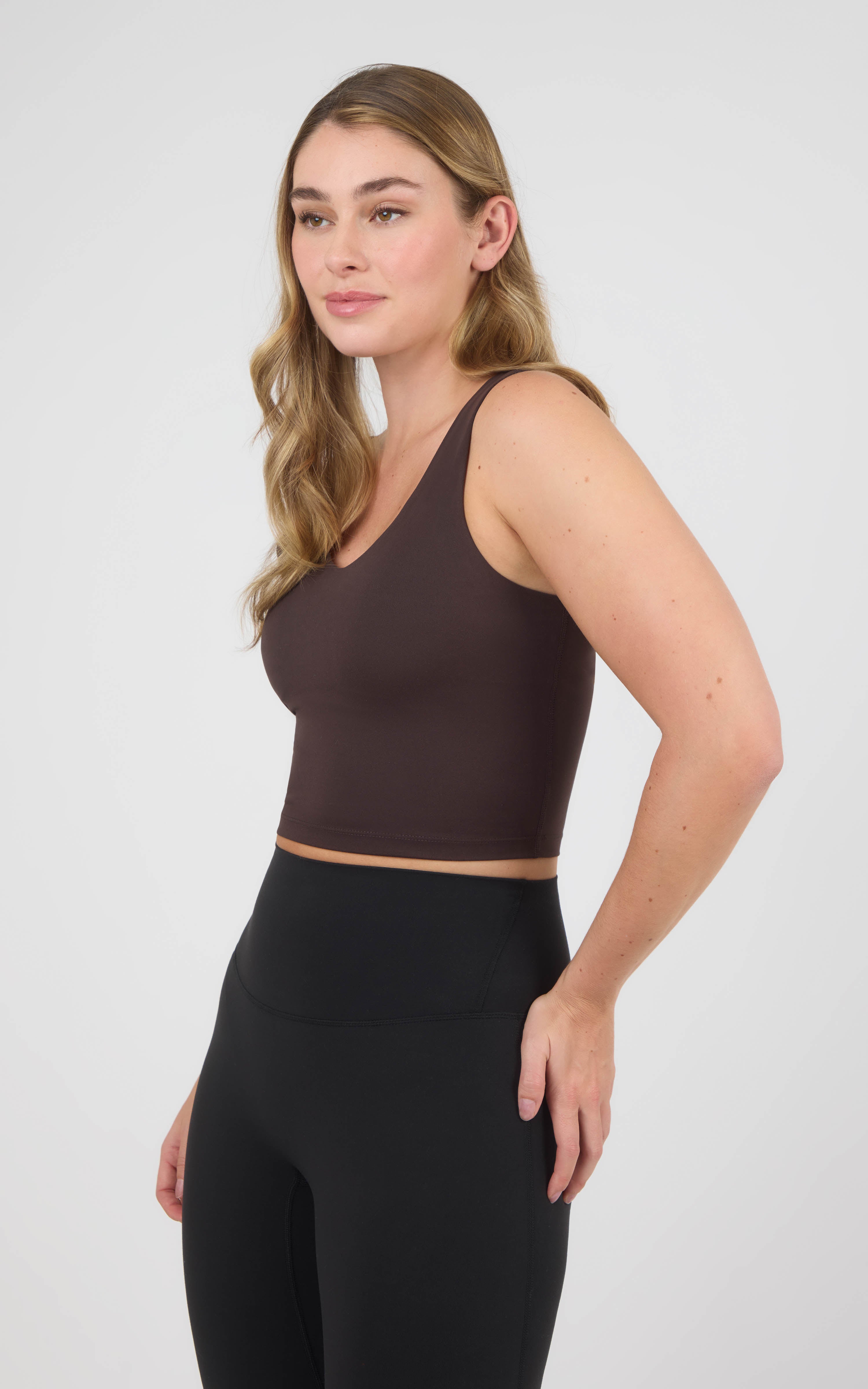 Woman wearing a cropped chocolate-brown scoop-neck tank with wide straps and a built-in bra, paired with black leggings.