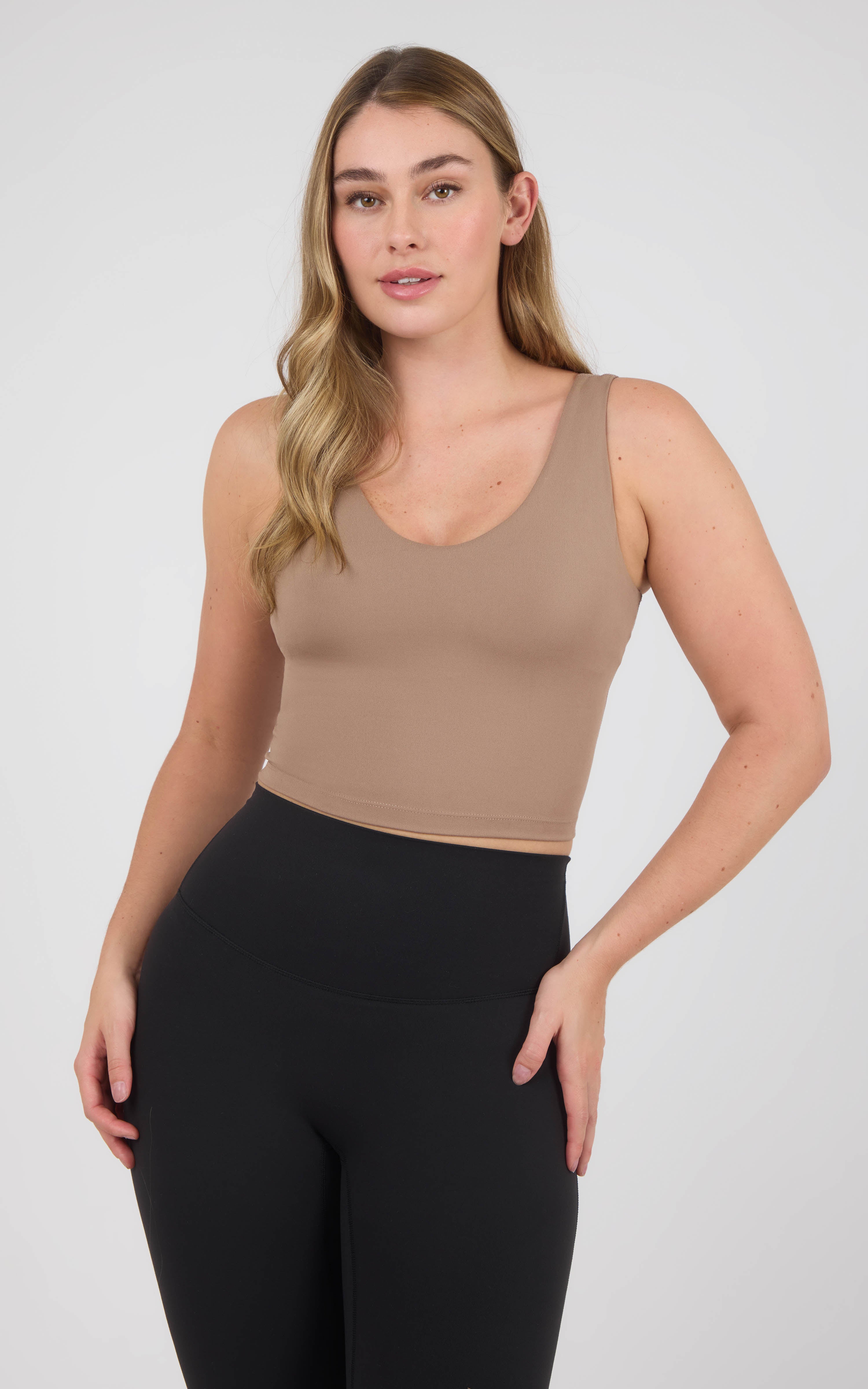 Woman wearing a taupe scoop-neck cropped tank with wide straps and a built-in bra, paired with black leggings.