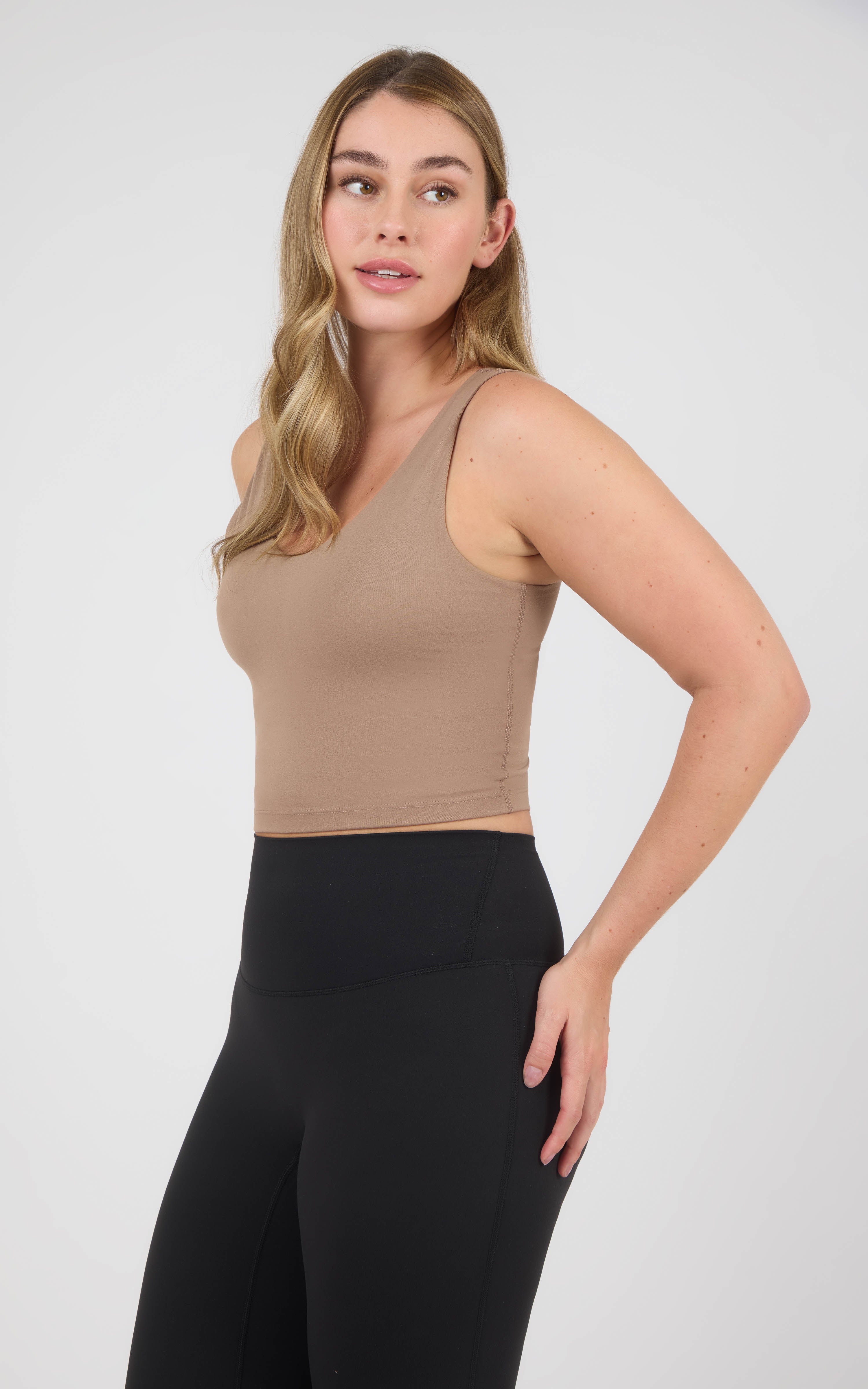 Woman wearing a cropped taupe scoop-neck tank with a built-in bra and high-waisted black leggings.