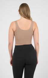 Back view of a beige cropped tank with a scoop neckline and wide straps, paired with black leggings.
