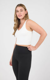 Woman wearing a white cropped scoop-neck tank with a built-in bra and black high-waisted leggings.