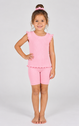 Little girl wearing a pink ribbed ruffle tank and matching biker shorts, with a pink scrunchie in her hair.