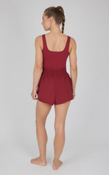 Sleeveless Tibetan Red short romper with square back neckline and cinched waist on barefoot woman viewed from behind.