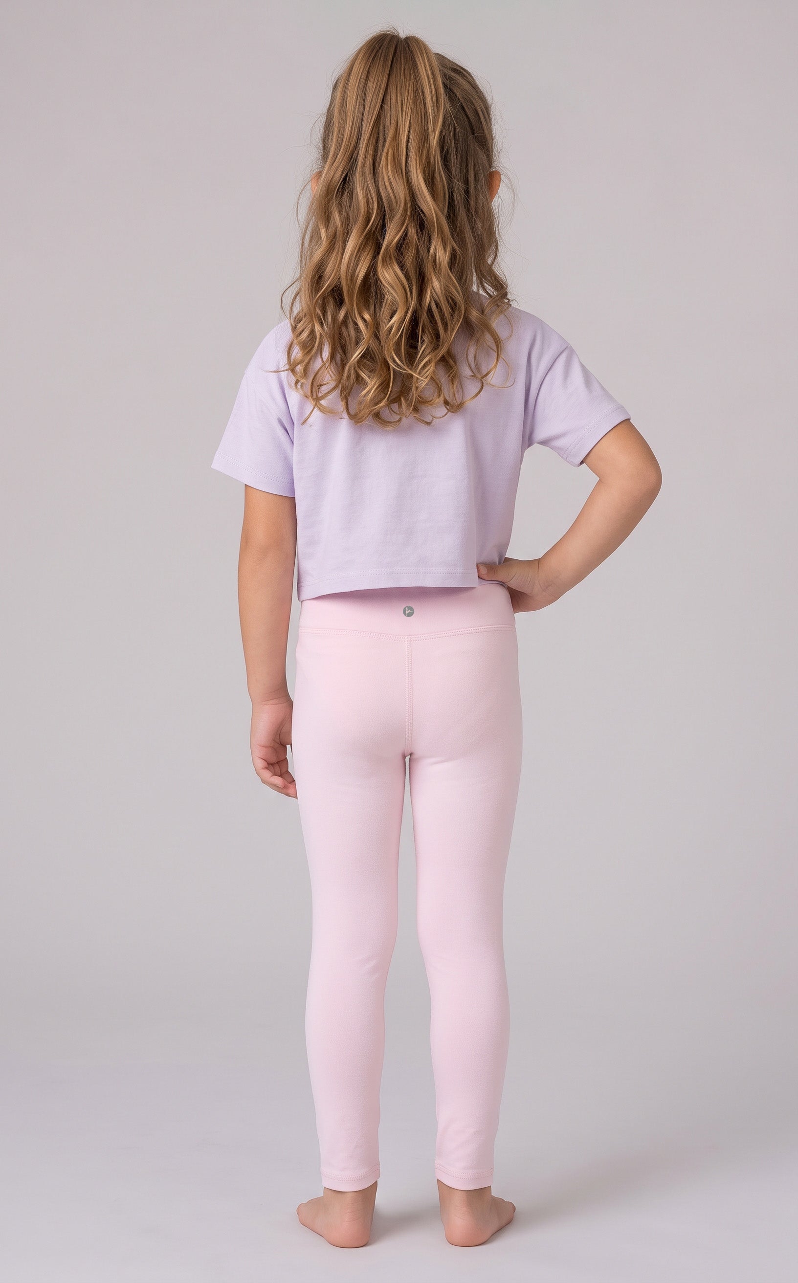 Back view of a girl wearing full-length pale pink leggings with a cropped lavender T-shirt.
