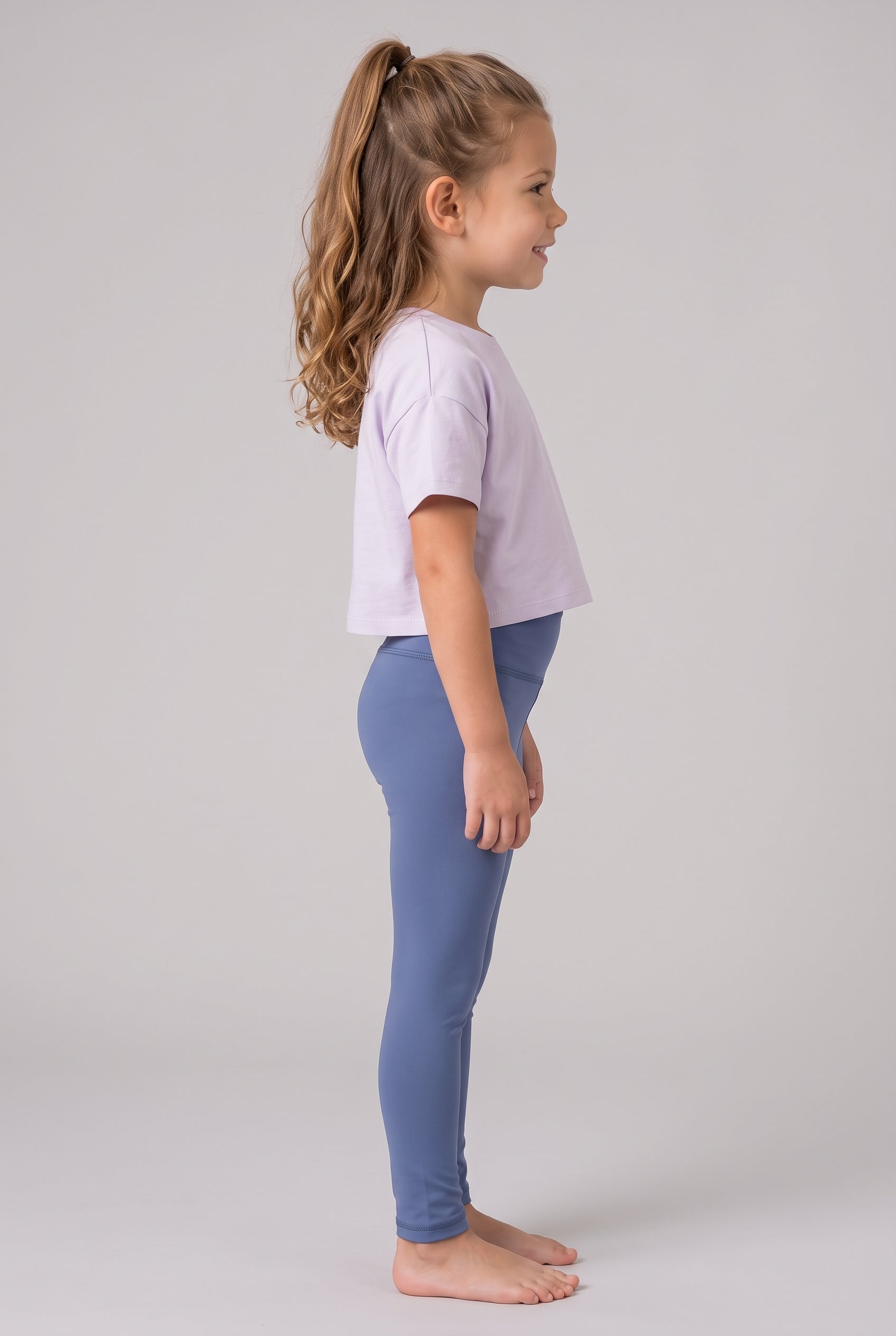 Little girl in profile wearing full-length blue leggings and a lavender short-sleeve shirt.