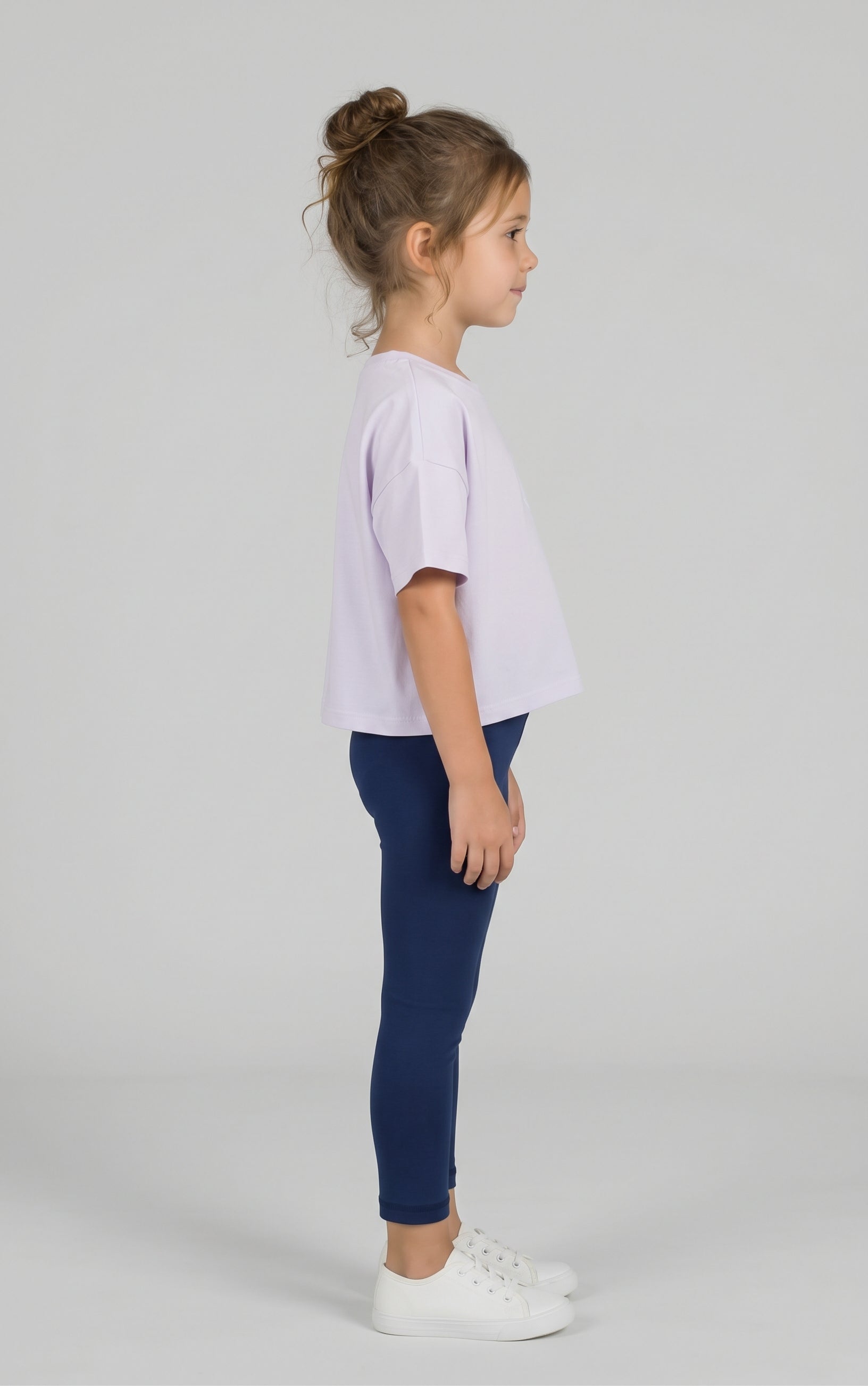 Toddler girl wearing navy leggings with a relaxed lavender tee and white sneakers, shown in profile.