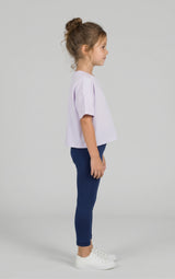 Toddler girl wearing navy leggings with a relaxed lavender tee and white sneakers, shown in profile.