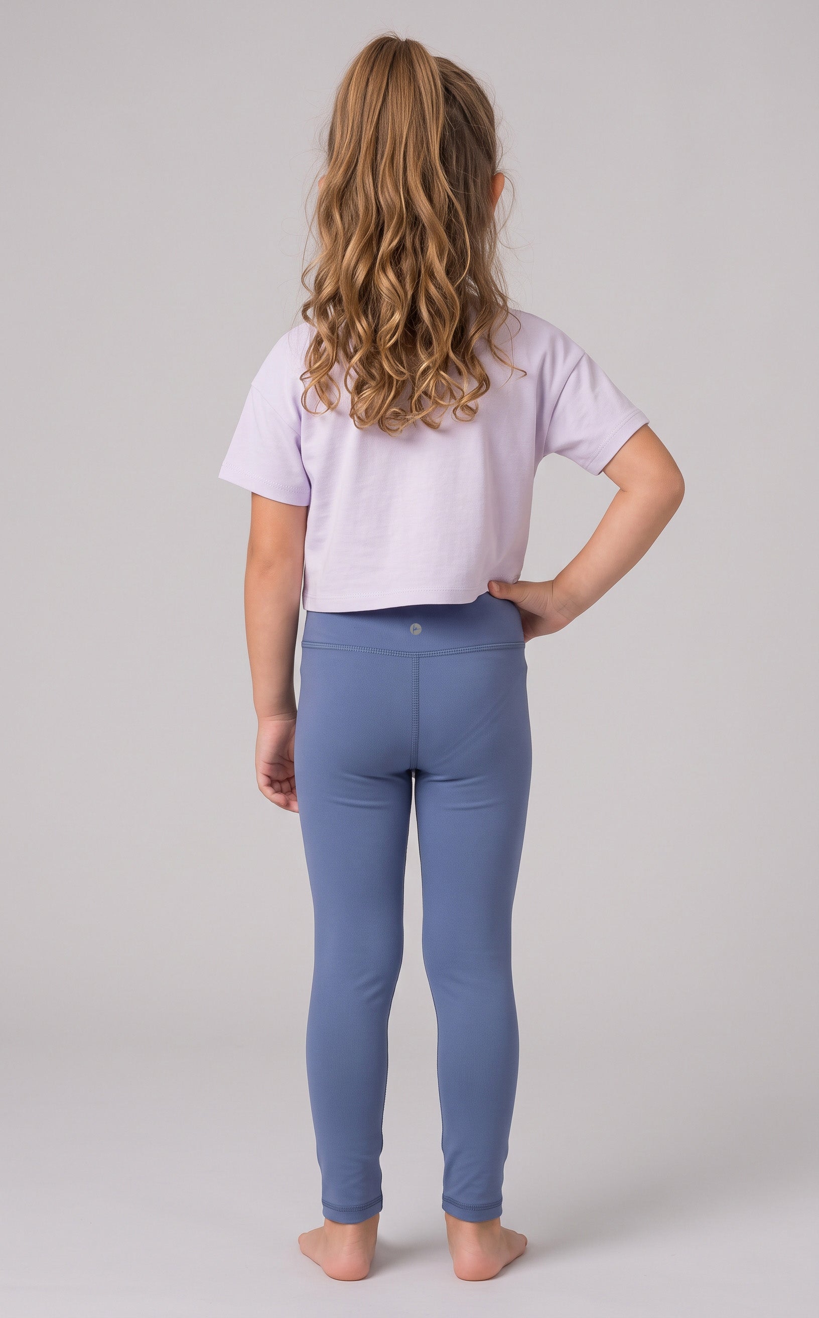 Little girl modeling full-length slate blue leggings with a fitted, stretchy look, shown from behind.