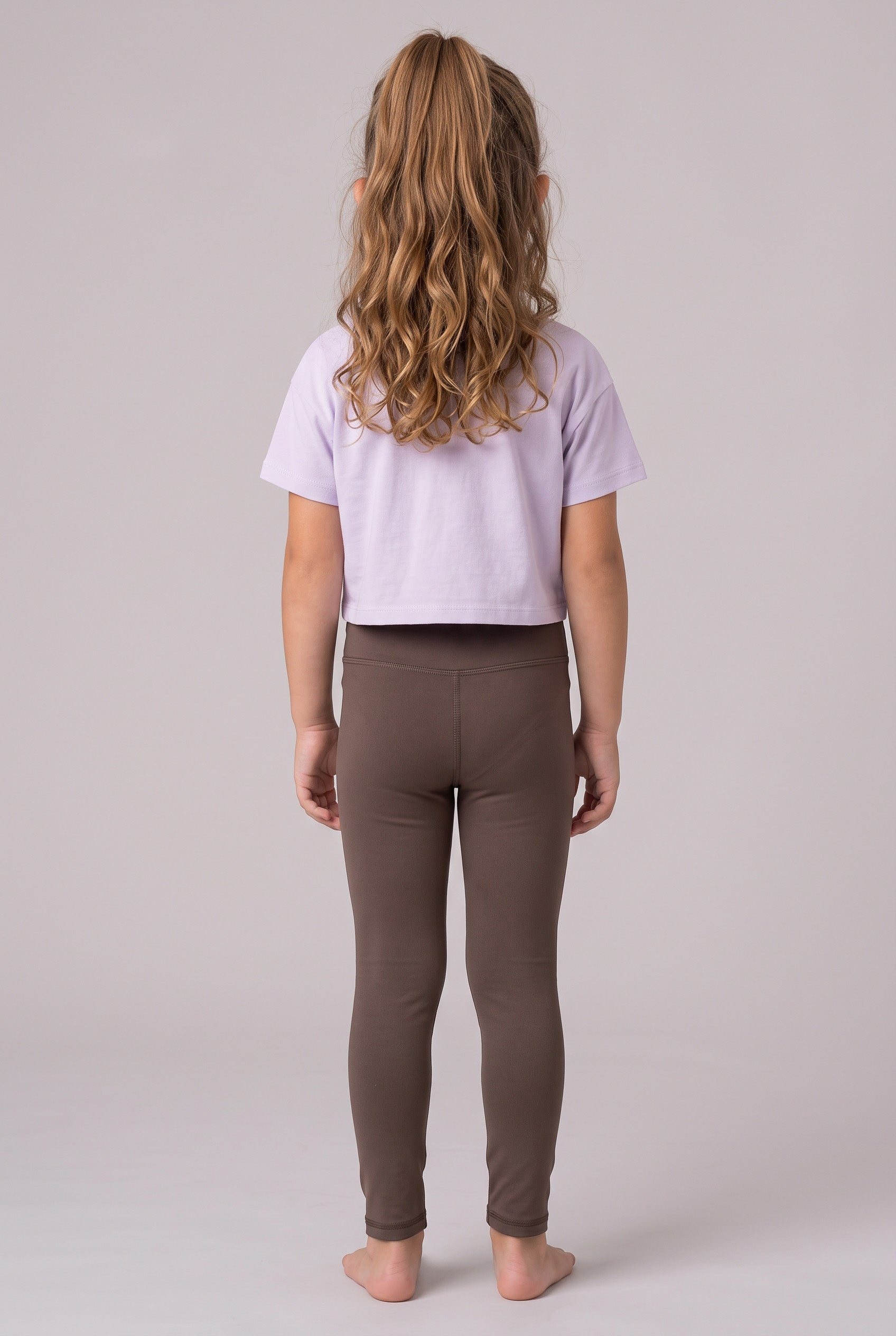 Back view of a girl wearing full-length dark taupe leggings with a soft, fitted stretch fabric and a lavender cropped.