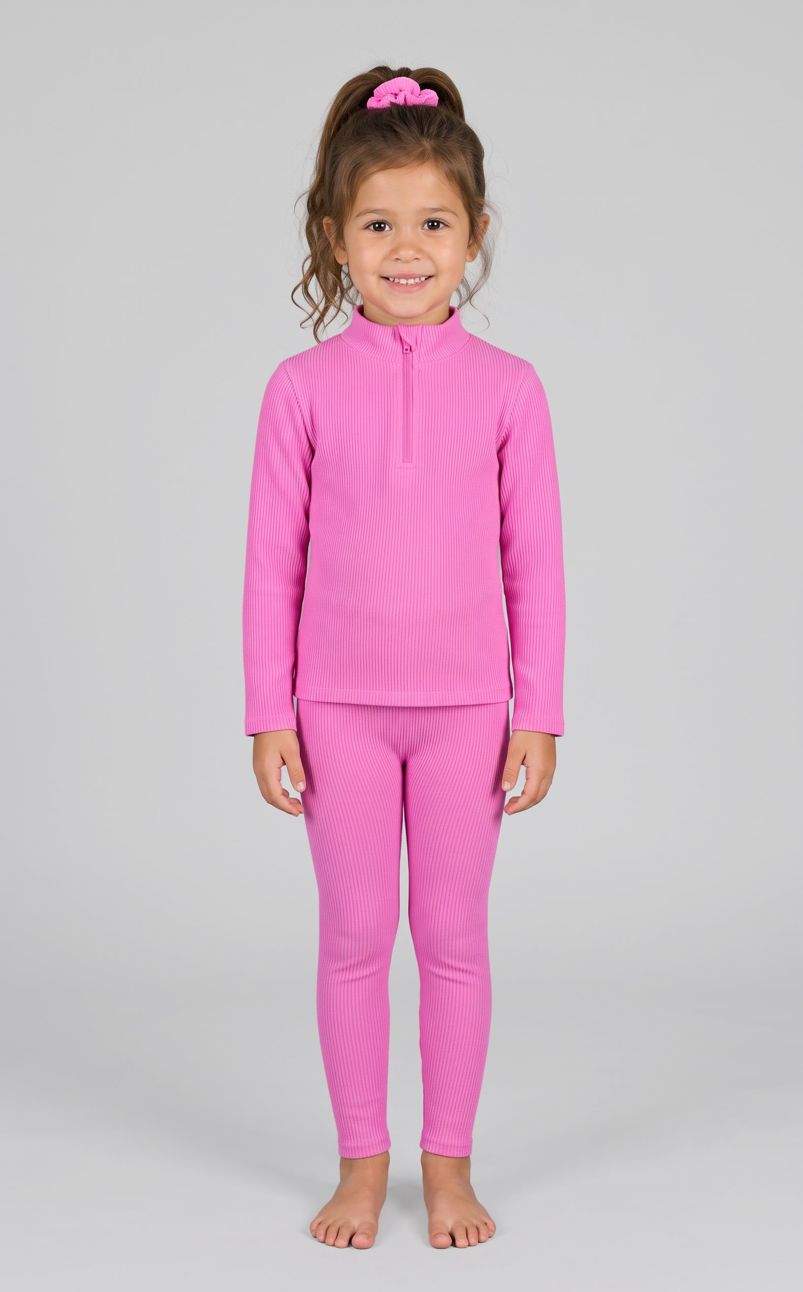 Little girl wearing a bright pink ribbed half-zip long sleeve top and matching leggings with a pink scrunchie in her hair.