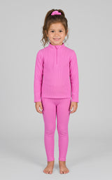 Little girl wearing a bright pink ribbed half-zip long sleeve top and matching leggings with a pink scrunchie in her hair.